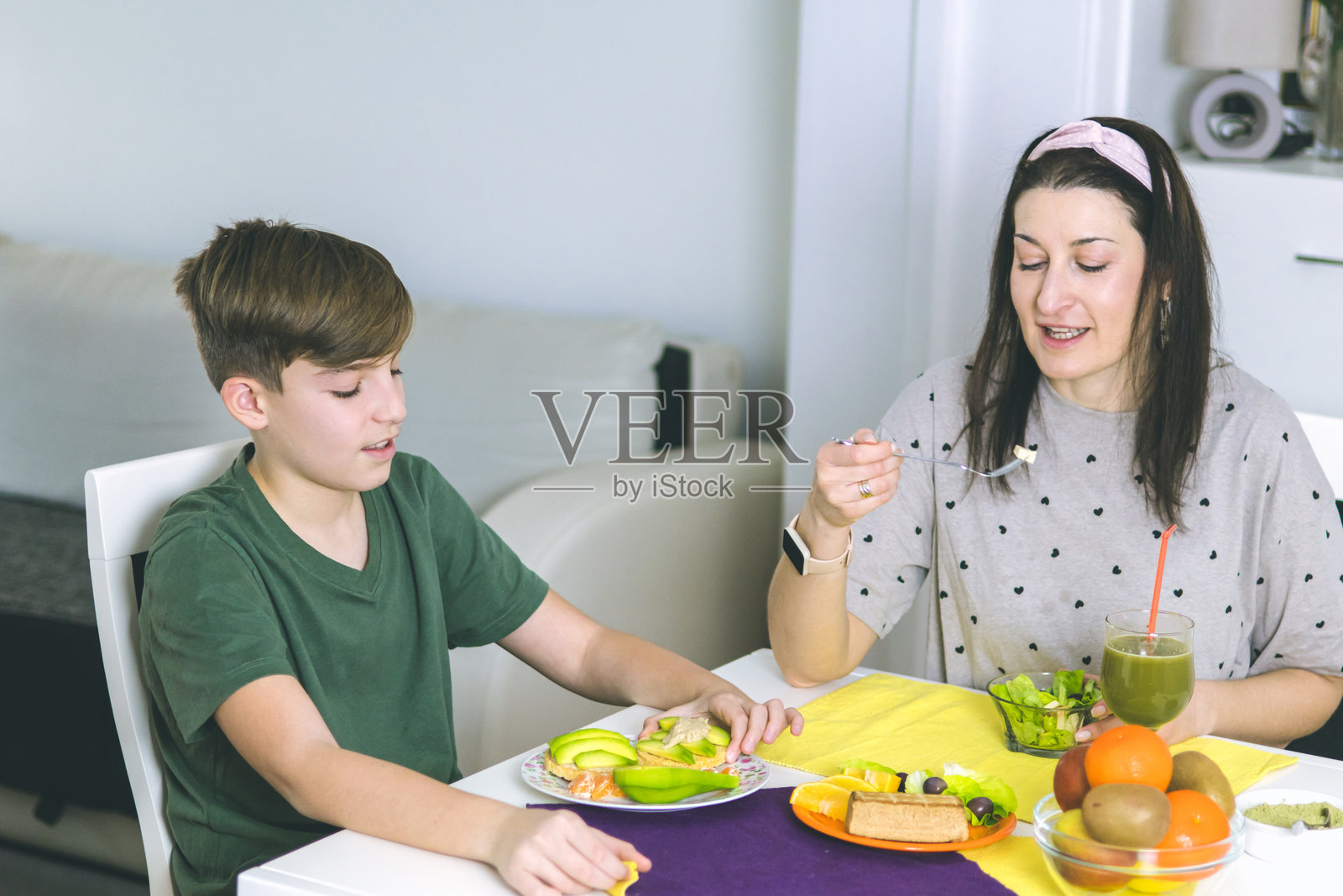 母亲和儿子在家中享受准备健康早餐的时光。早餐的超级食材包括螺旋藻、熏豆腐、鳄梨、生菜、米饼和水果。照片摄影图片