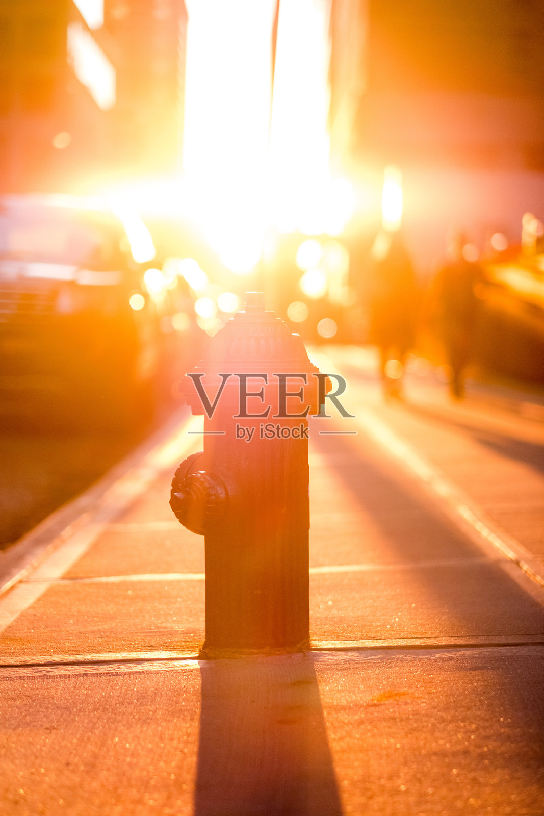 城市街道上的日落,消防栓在温暖的光线中投射出长长的影子,映衬出繁忙的城市景观。照片摄影图片