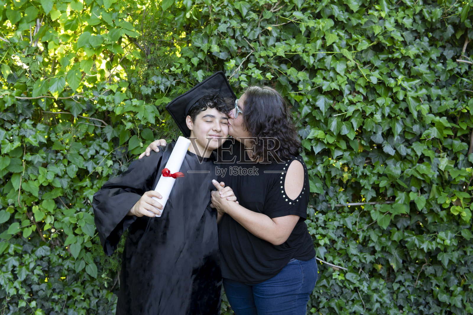 年轻的刚毕业男孩,身穿学士服,手持学位证书,与家人一起庆祝照片摄影图片
