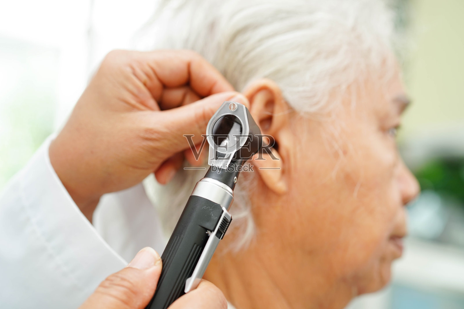 耳鼻喉科医生使用耳镜检查老年患者的耳朵,解决听力损失问题。照片摄影图片