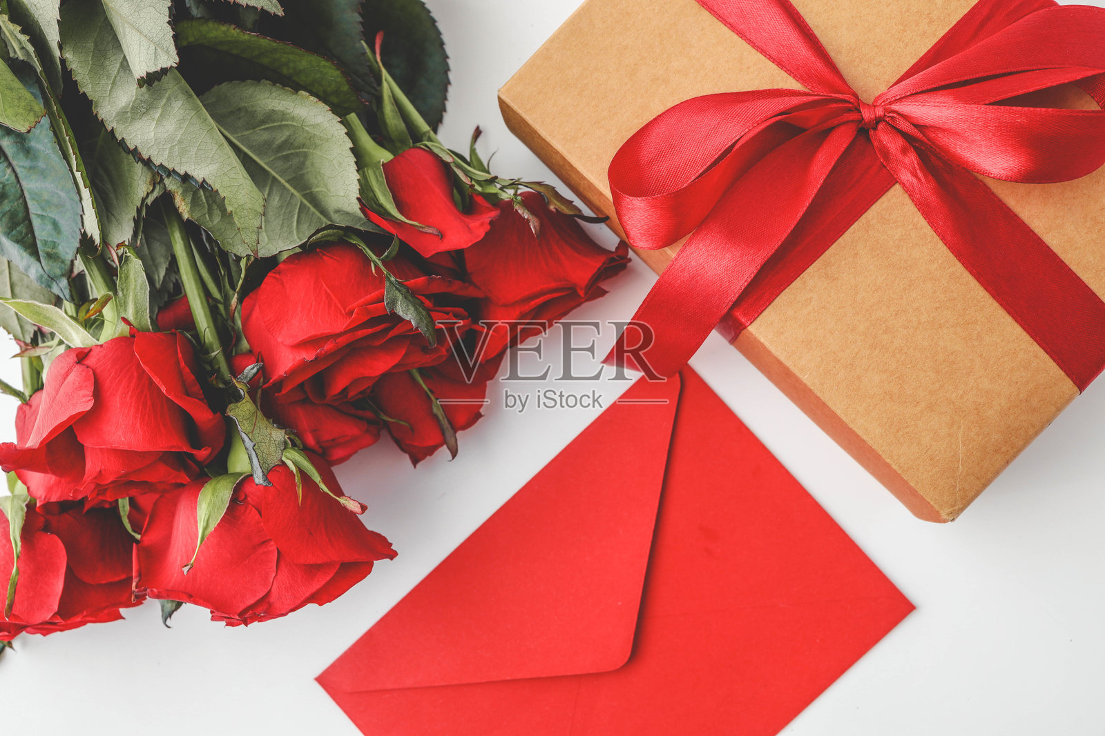 一束红玫瑰、一封红包和一个装饰有缎带的礼品盒,构成了一个节日而浪漫的平铺构图,完美适合情人节、周年纪念或特殊场合。照片摄影图片
