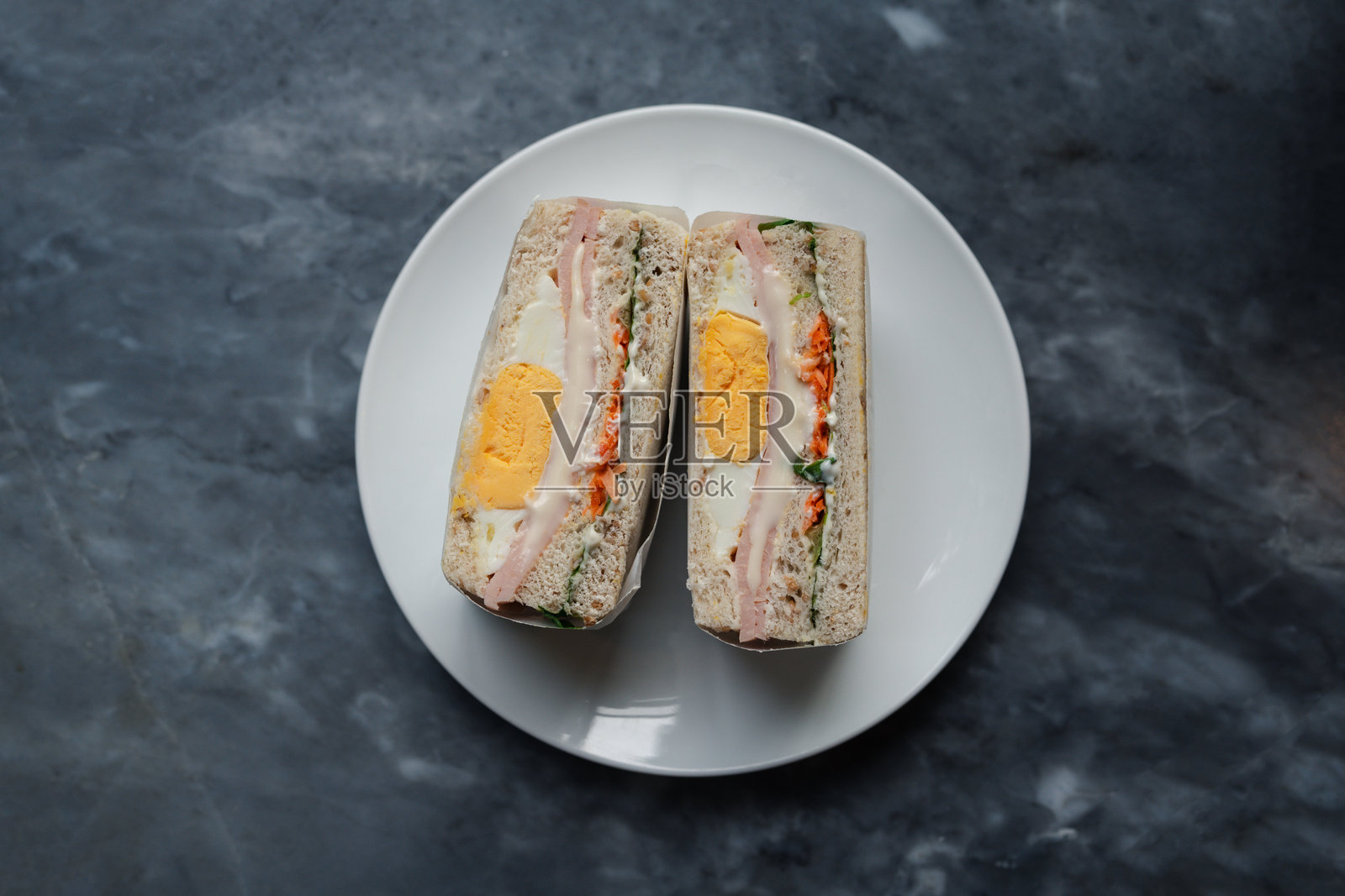 从上方看新鲜制作的三明治半边,夹有煮鸡蛋、火腿和蔬菜,放在柔软的面包上,包装好以便食用,适合早餐、午餐或休闲场合的健康小吃选择。照片摄影图片