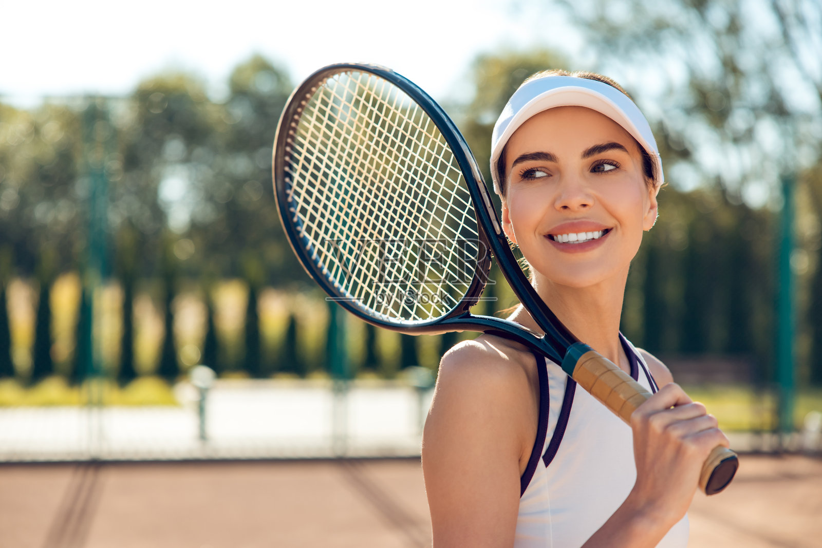 微笑的瘦女人在网球场上站着,手持球拍,享受户外夏季锻炼。照片摄影图片