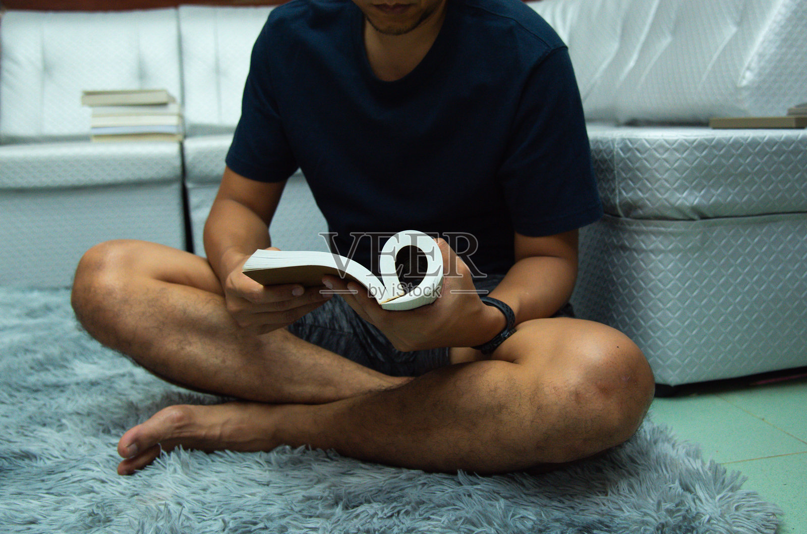 一名男子舒适地坐在沙发上,专心阅读一本书。他的穿着休闲而整洁,比如衬衫和长裤,暗示着在宁静环境中享受悠闲时光。照片摄影图片