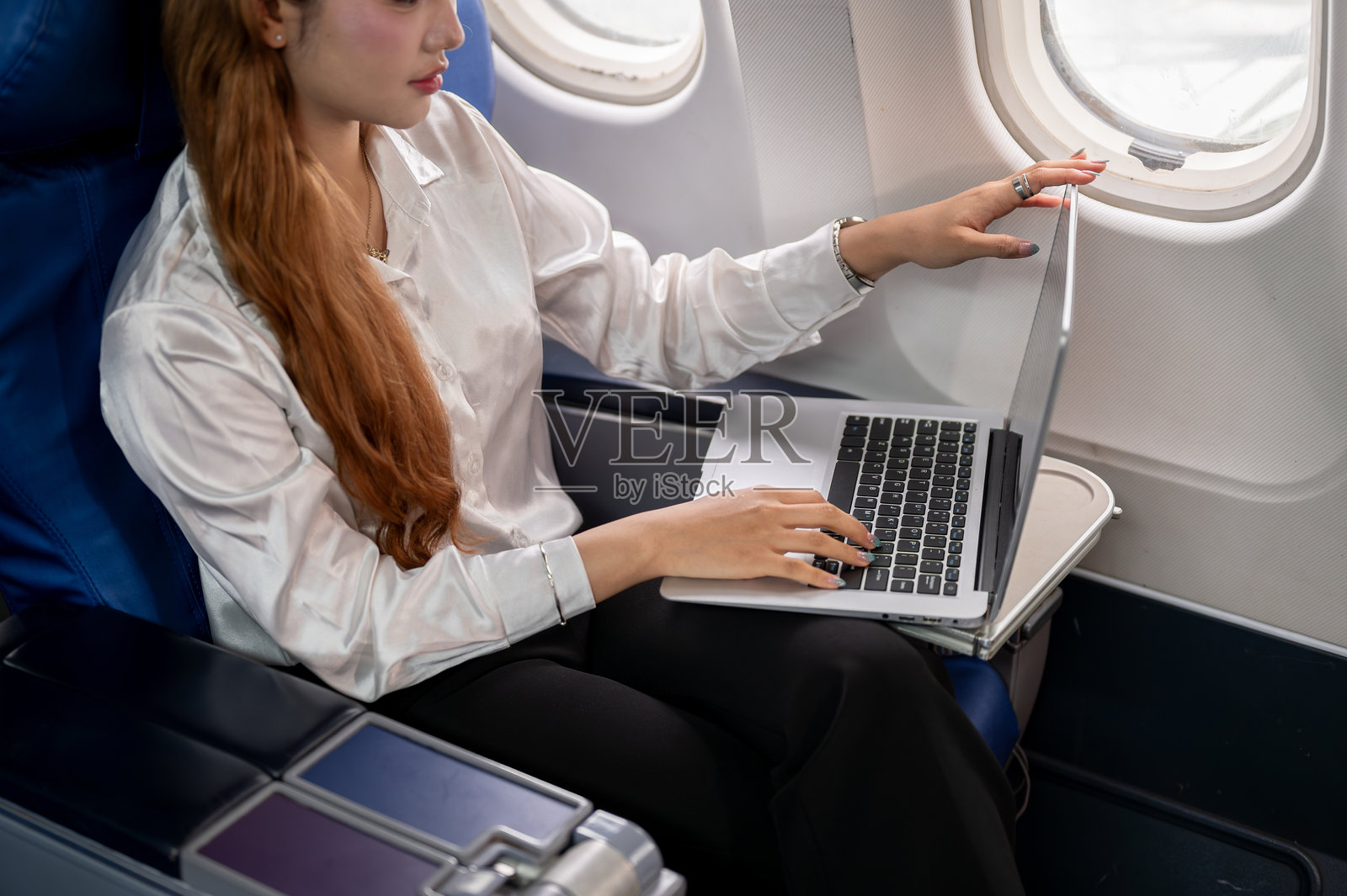 一位女商人在飞机上工作,特写镜头显示她正在笔记本电脑键盘上打字。照片摄影图片