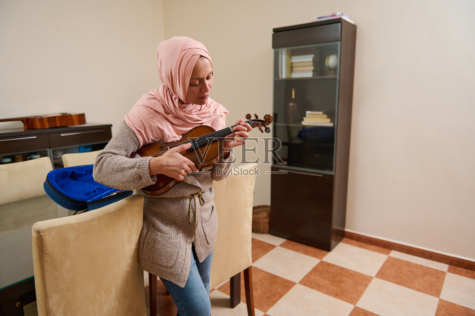 戴头巾的女性在温馨的客厅里练习小提琴照片摄影图片