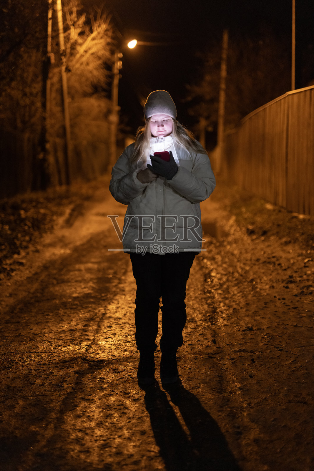 年轻女性在夜晚独自走在安静昏暗的街道上,手中的智能手机照亮了周围,营造出一种古朴而宁静的氛围。照片摄影图片