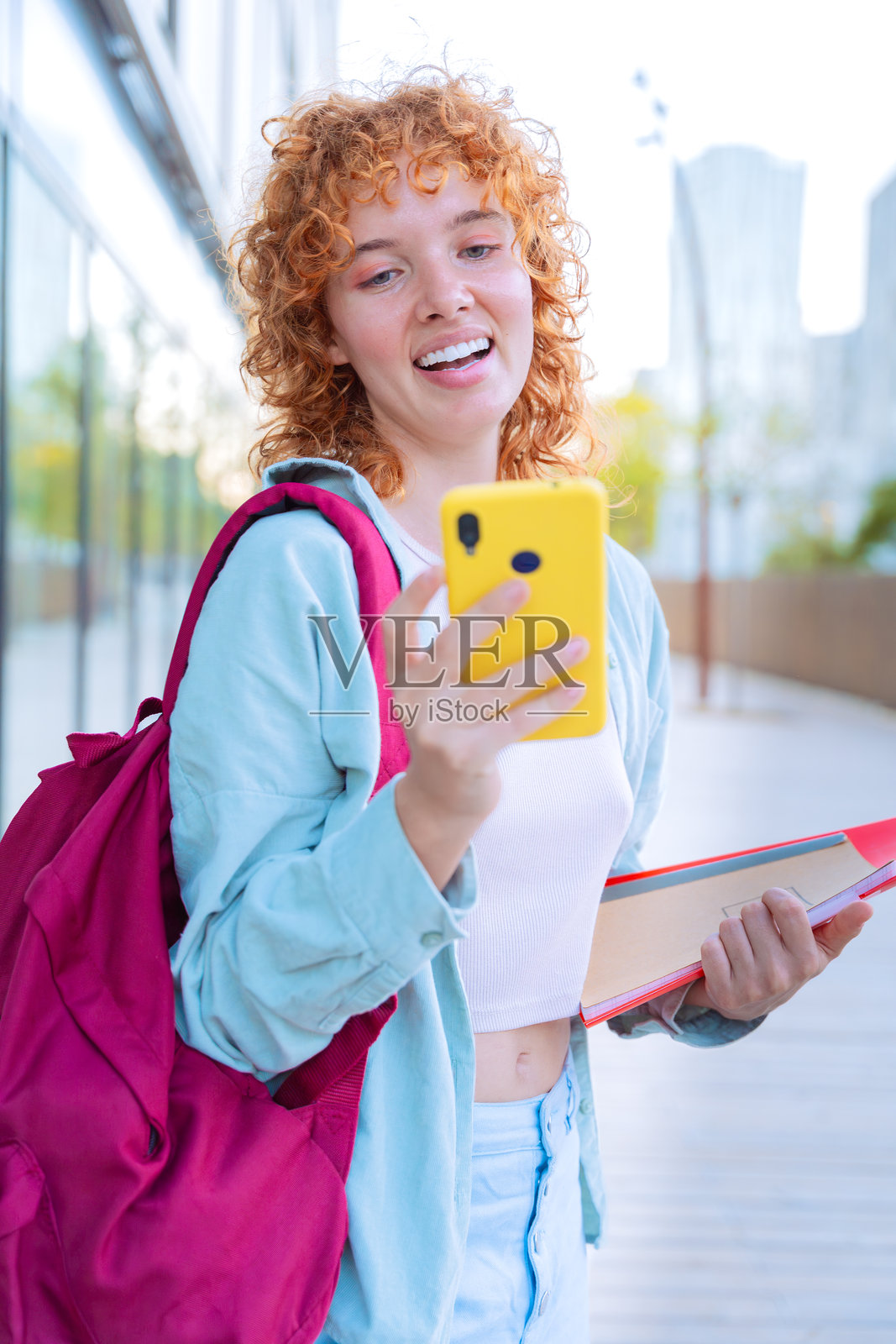 微笑的年轻女性在户外穿着休闲服装,手持智能手机和笔记本。照片摄影图片