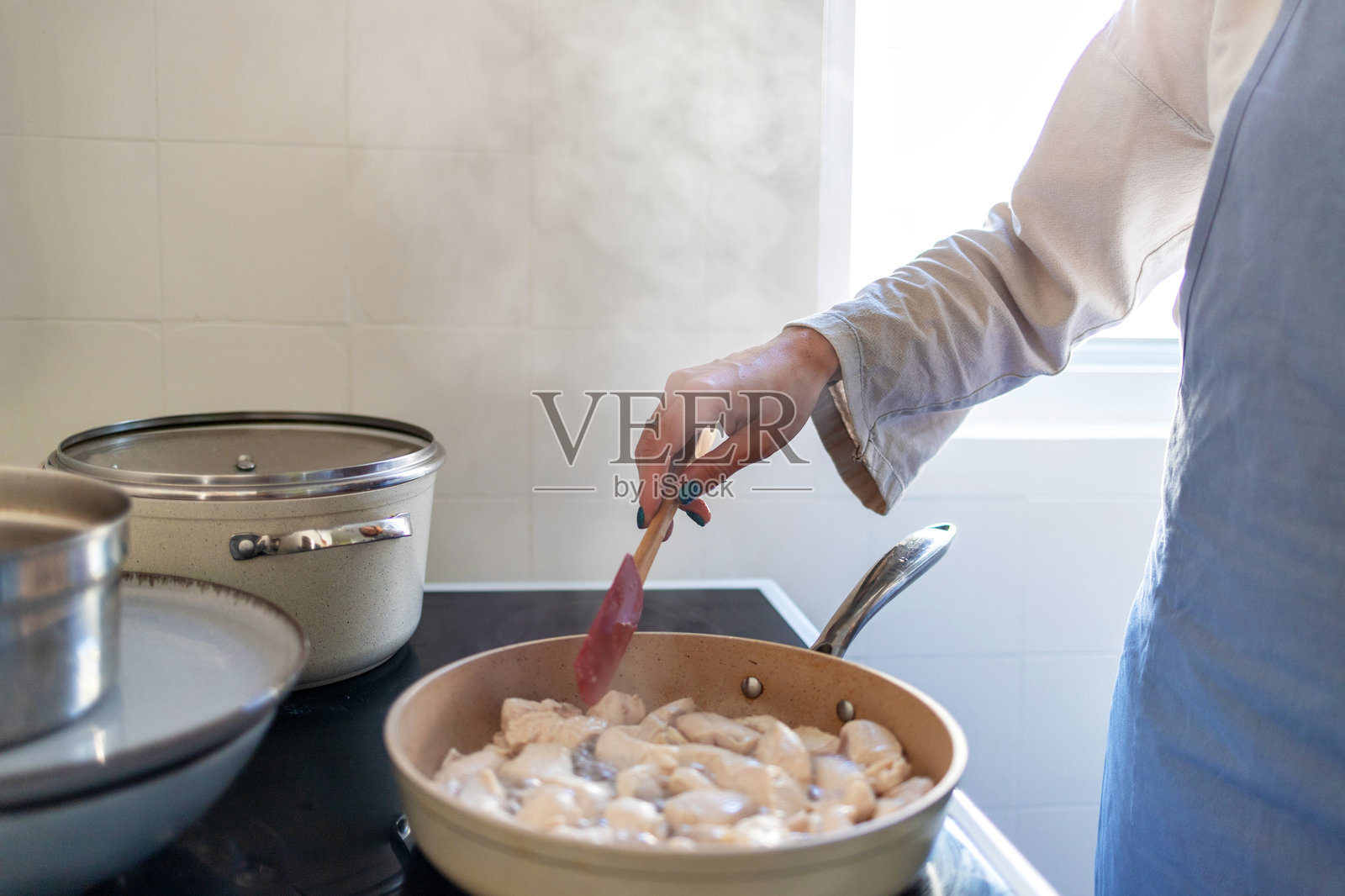 一位女性的手用硅胶铲在锅中翻炒鸡胸肉片。照片摄影图片