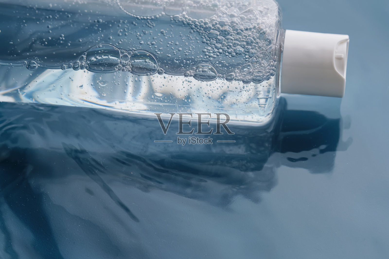 蓝色背景下水中漂浮的面部和身体用化妆凝胶瓶。照片摄影图片