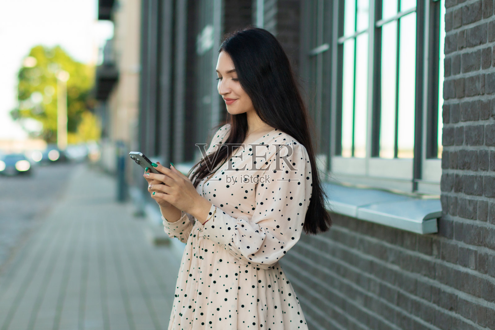 穿着波点裙的时尚女性在户外使用智能手机——现代沟通、时尚生活方式和城市优雅。照片摄影图片