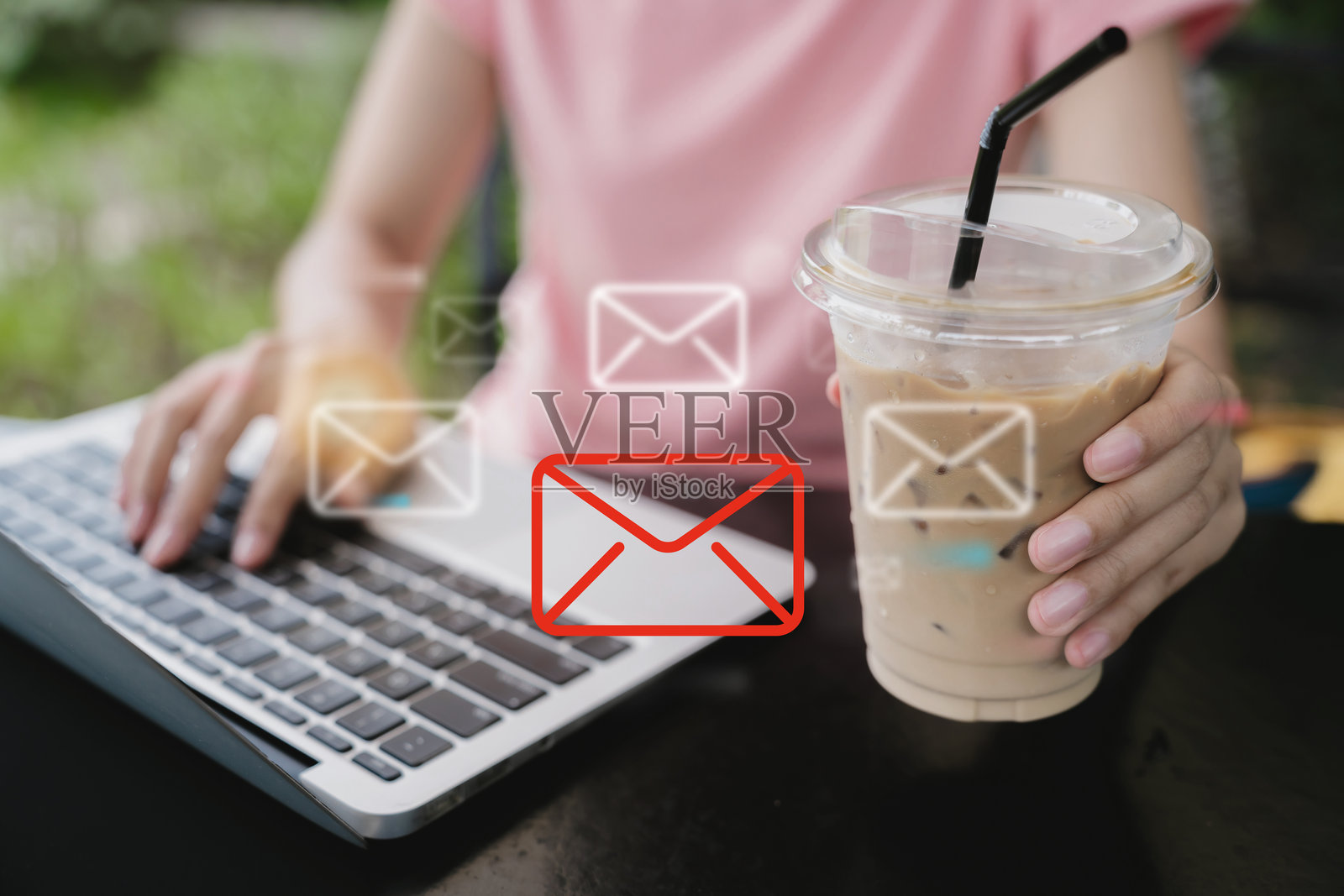 在休闲的户外环境中,一个人一边打字一边拿着冰咖啡杯。照片摄影图片