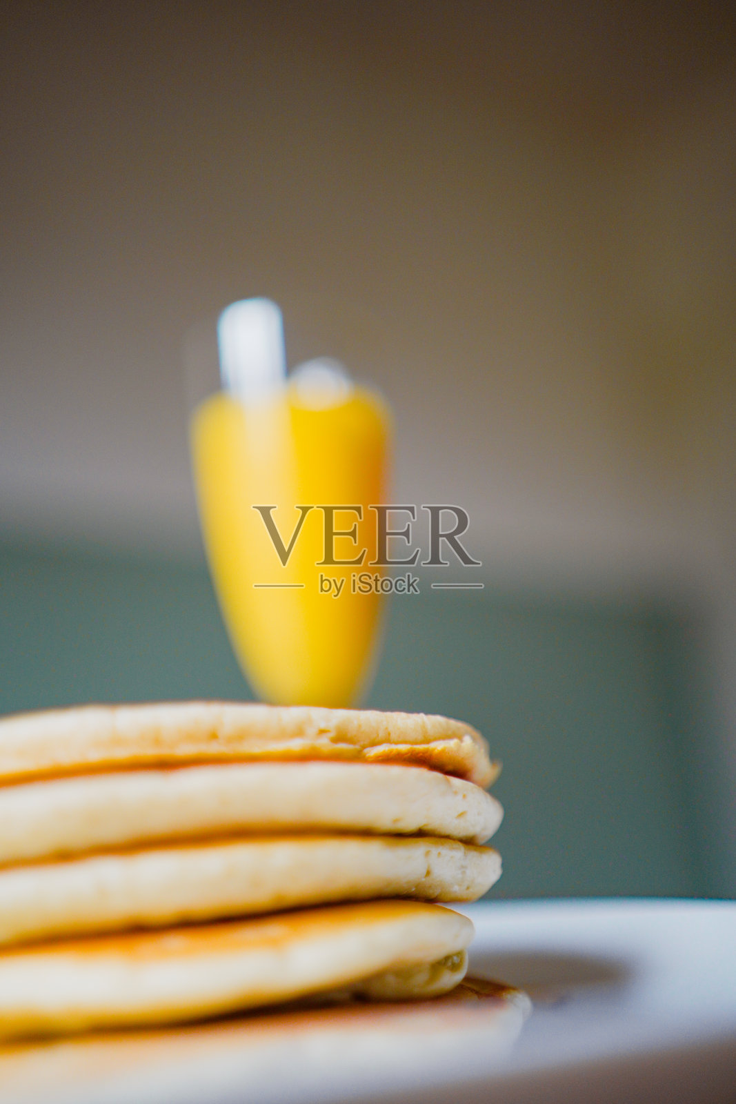 一堆淋有糖浆的煎饼,背景是橙汁,完美的早餐场景照片摄影图片