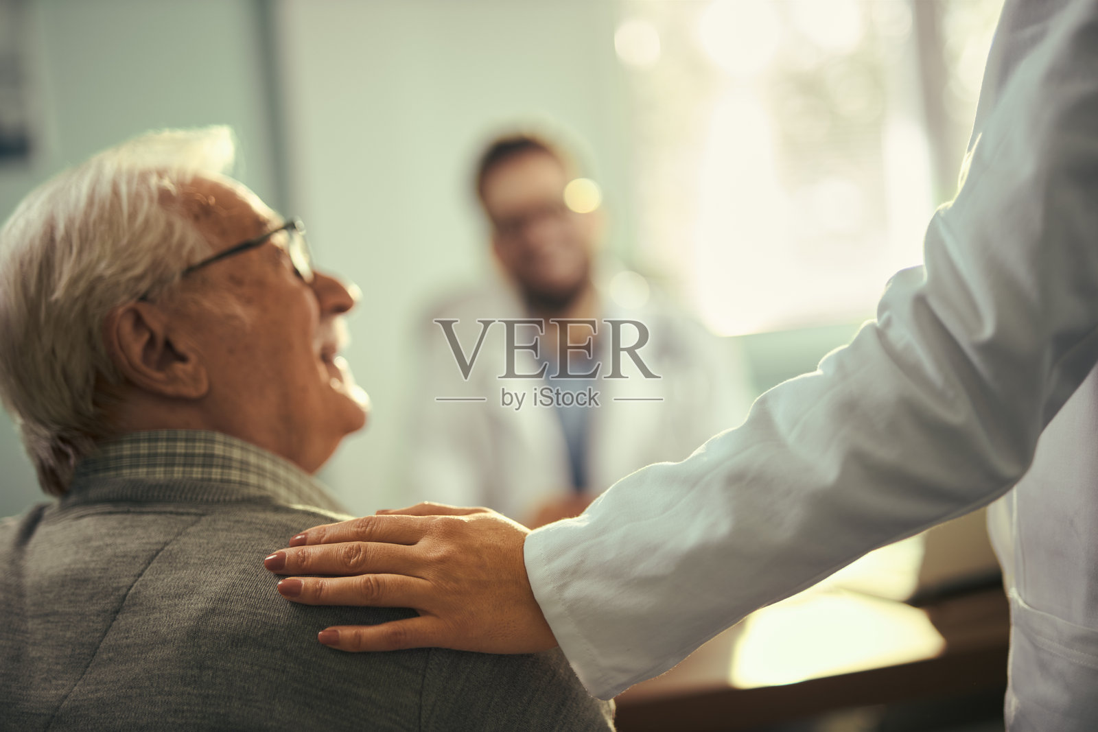 微笑的成熟男性在办公室与医生交谈。照片摄影图片