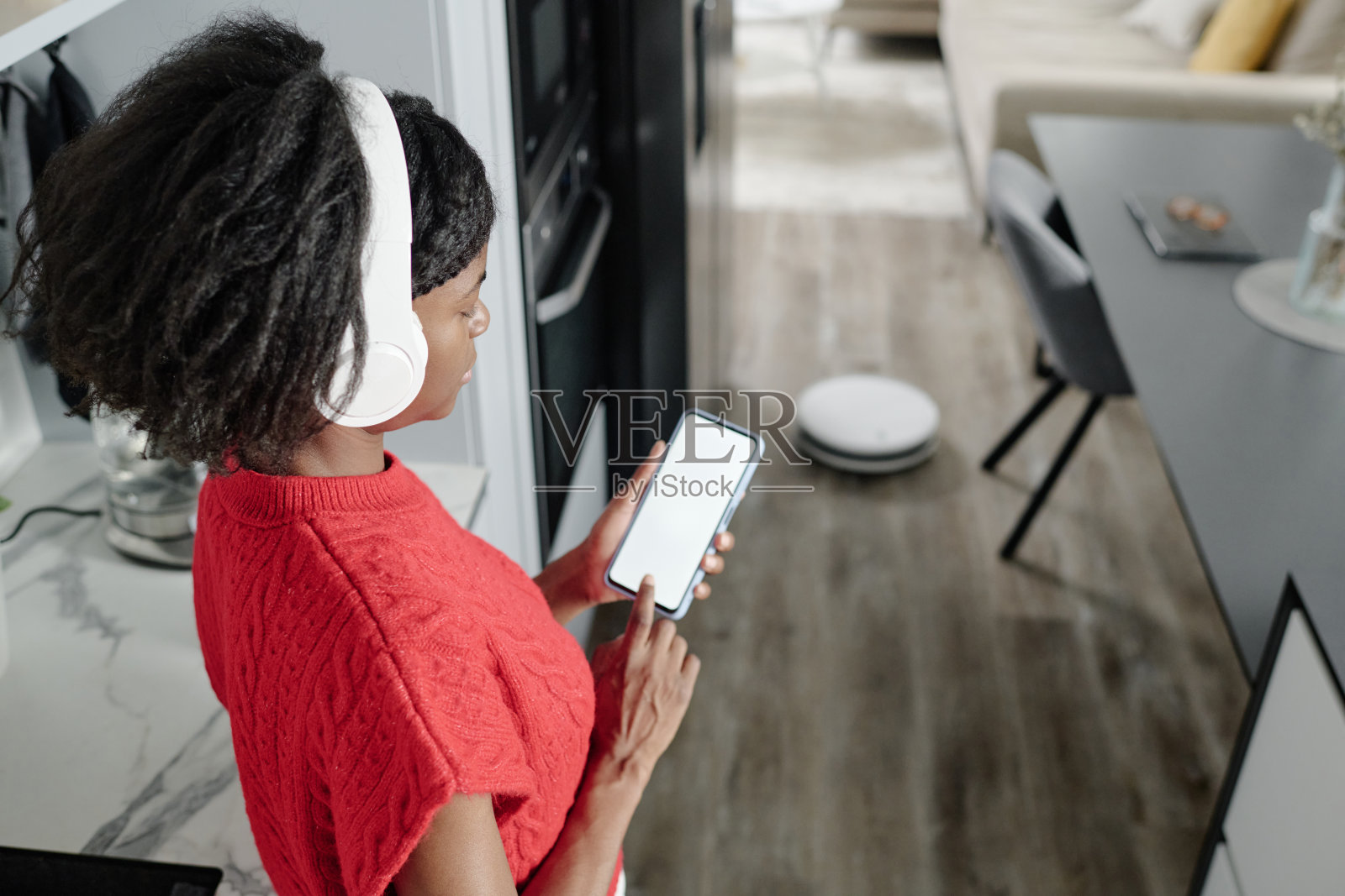 戴着耳机的女性在做家务,旁边有机器人清洁器照片摄影图片