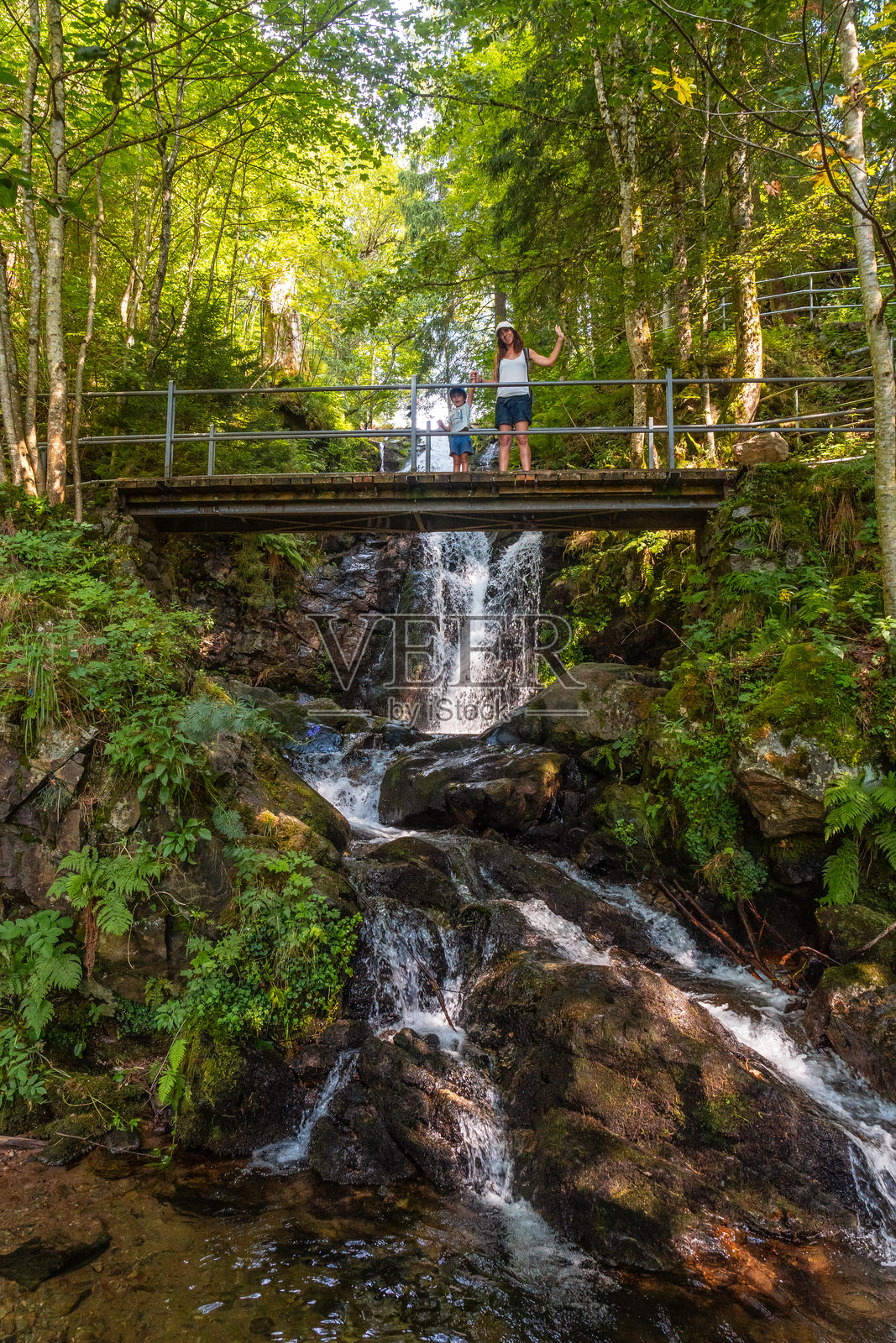 一位母亲和她的儿子在德国黑森林的托特瑙瀑布桥上挥手。照片摄影图片