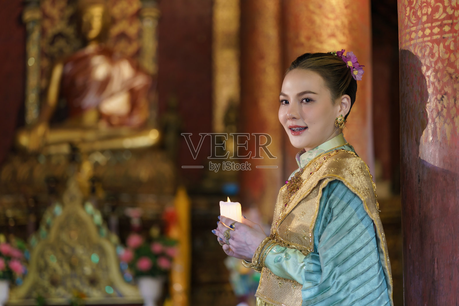 一位优雅着装的泰国女性在寺庙中安静地站立,手中点燃的蜡烛照亮了周围的空间。照片摄影图片