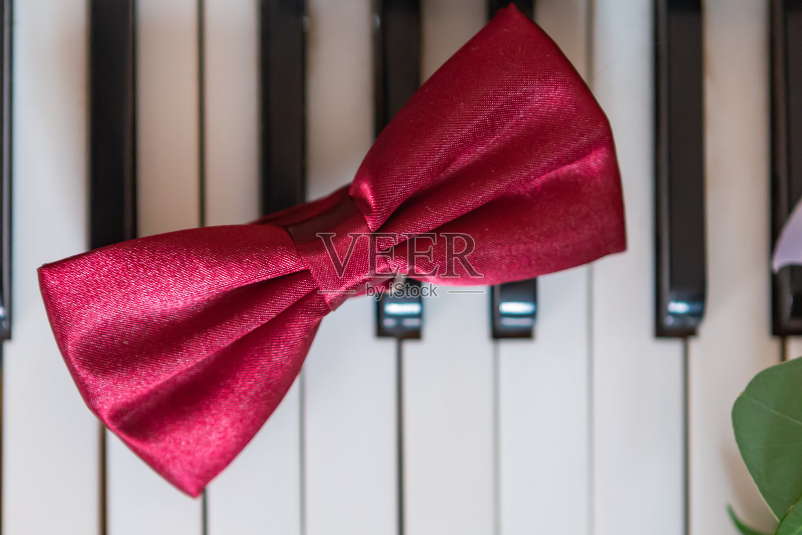红色缎面蝴蝶结静静地放在黑白钢琴键上,营造出时尚的氛围。照片摄影图片