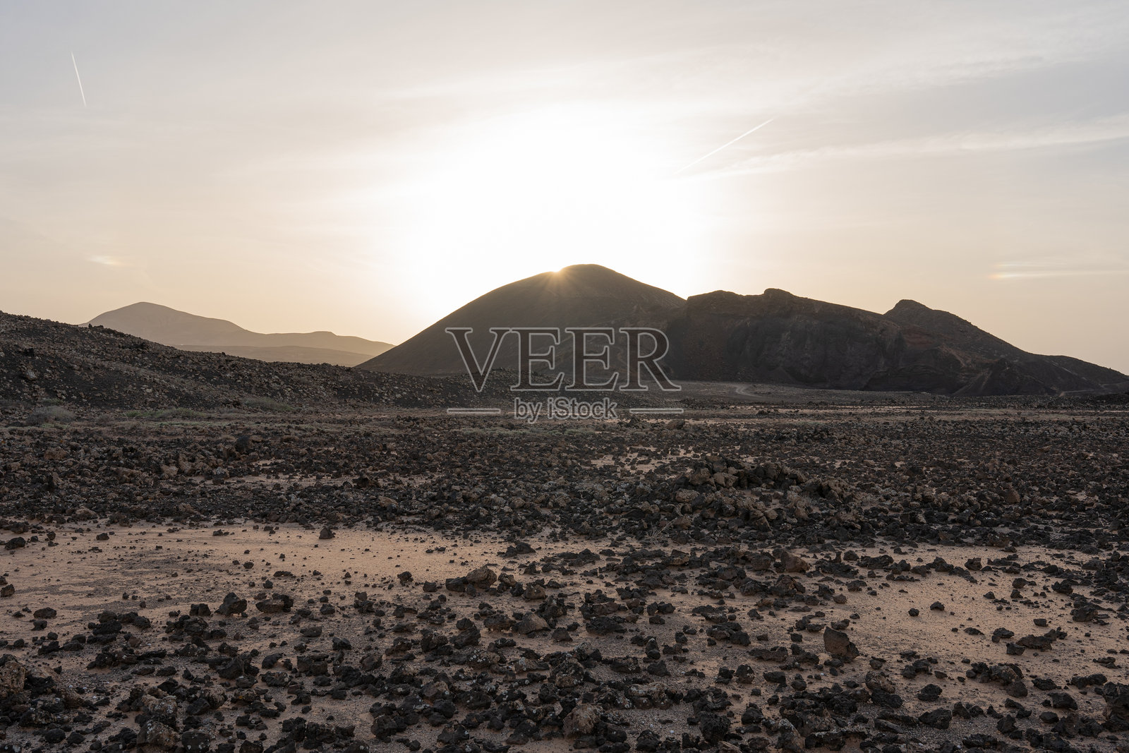 阳光在加那利群岛兰萨罗特的荒凉岩石景观中的火山后升起照片摄影图片