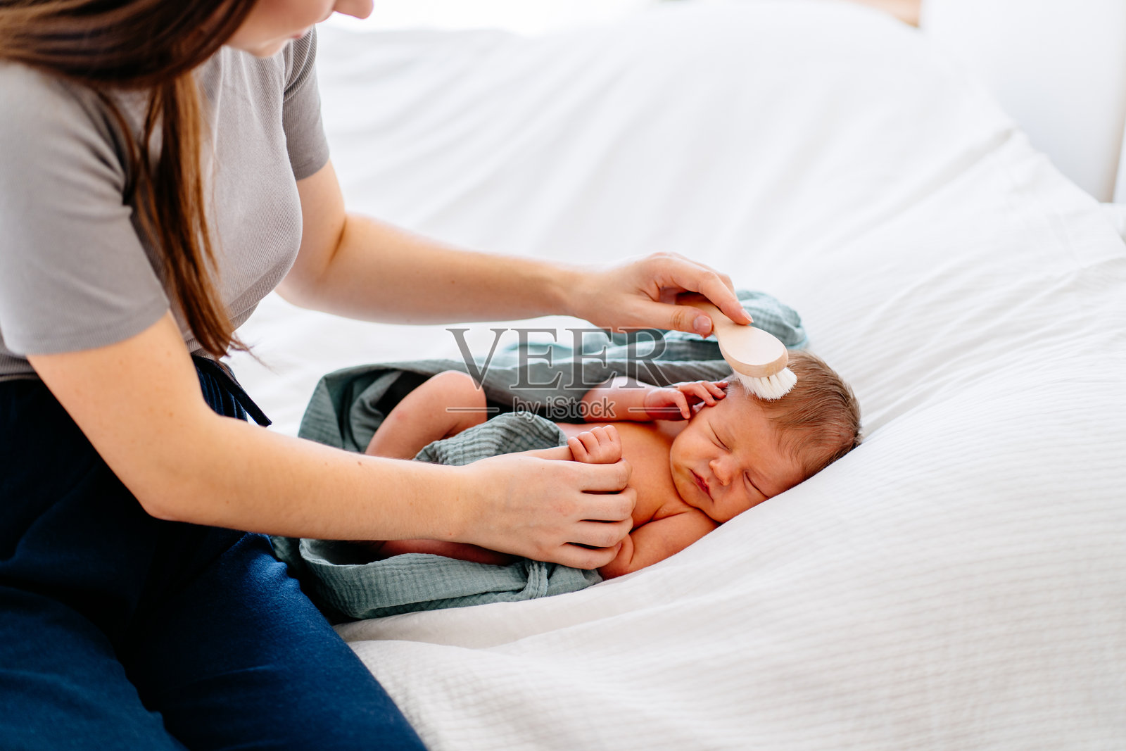 母亲轻柔地抚摸着在白色床上熟睡的新生儿照片摄影图片
