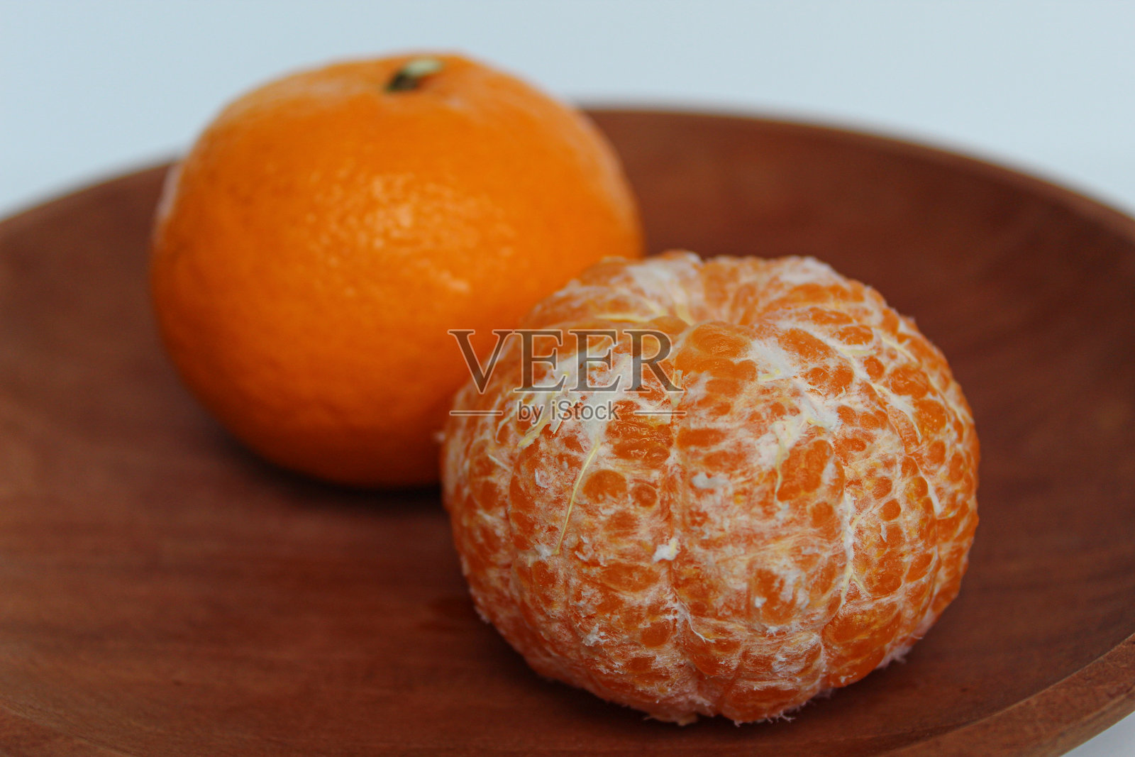 剥皮前后橙子的对比,放在木盘上,背景为白色。照片摄影图片