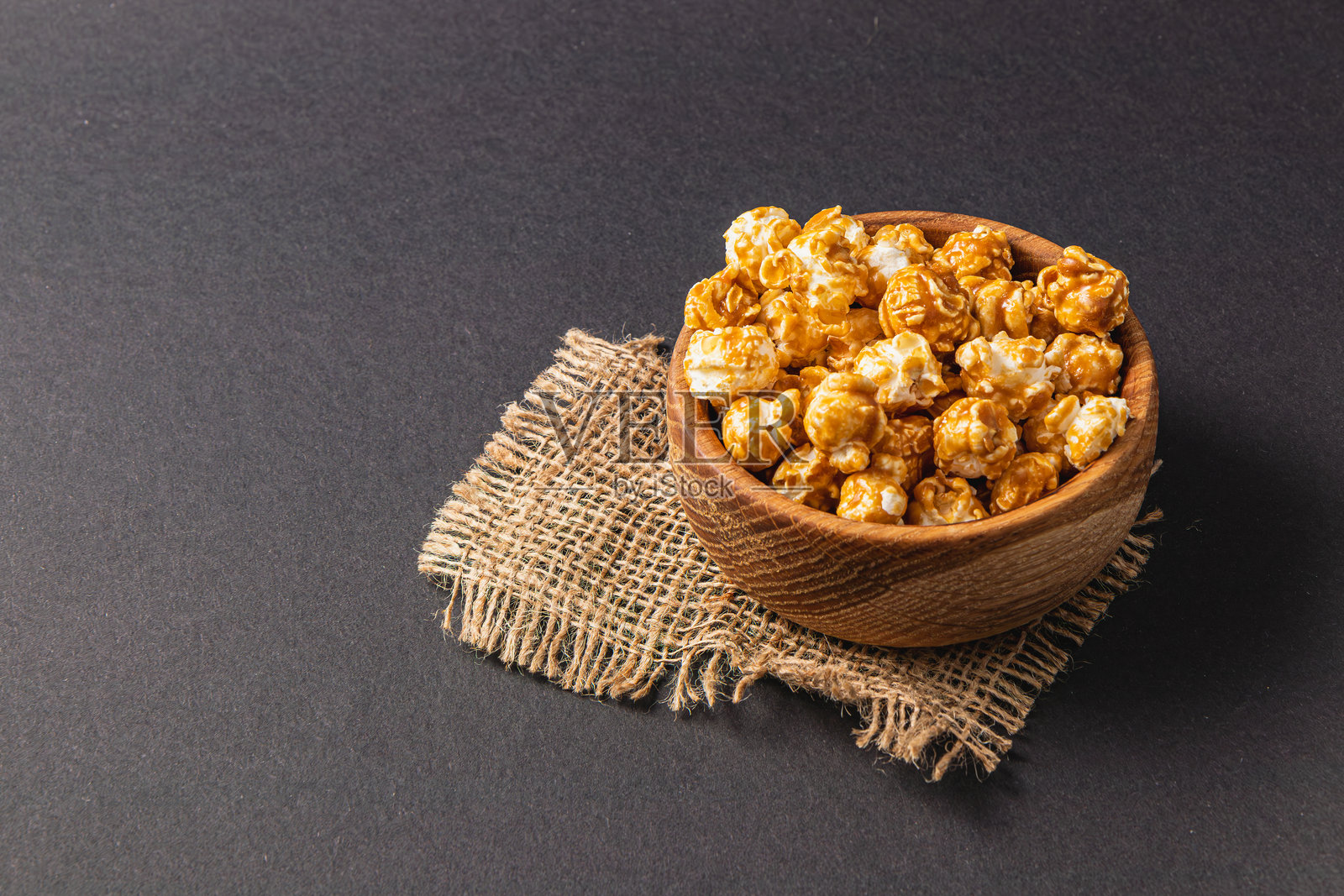 黑色背景上的木碗里盛着甜美的焦糖爆米花照片摄影图片