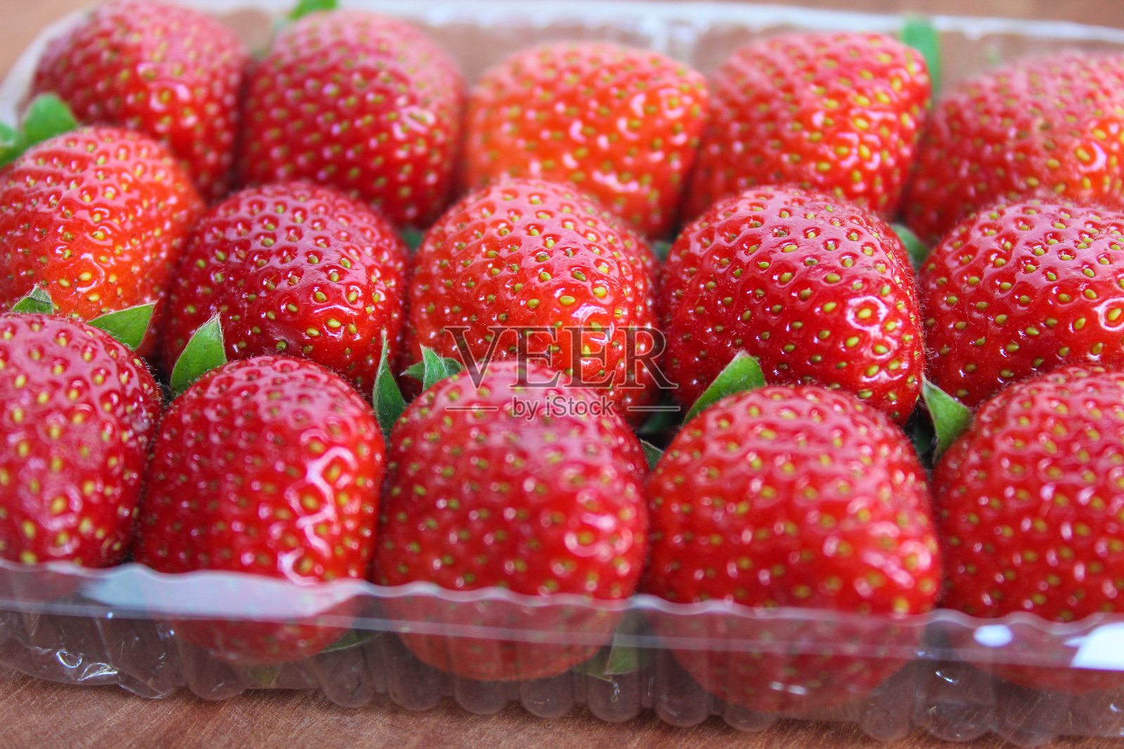 新鲜草莓装在塑料容器中,背景为木质表面特写图。照片摄影图片