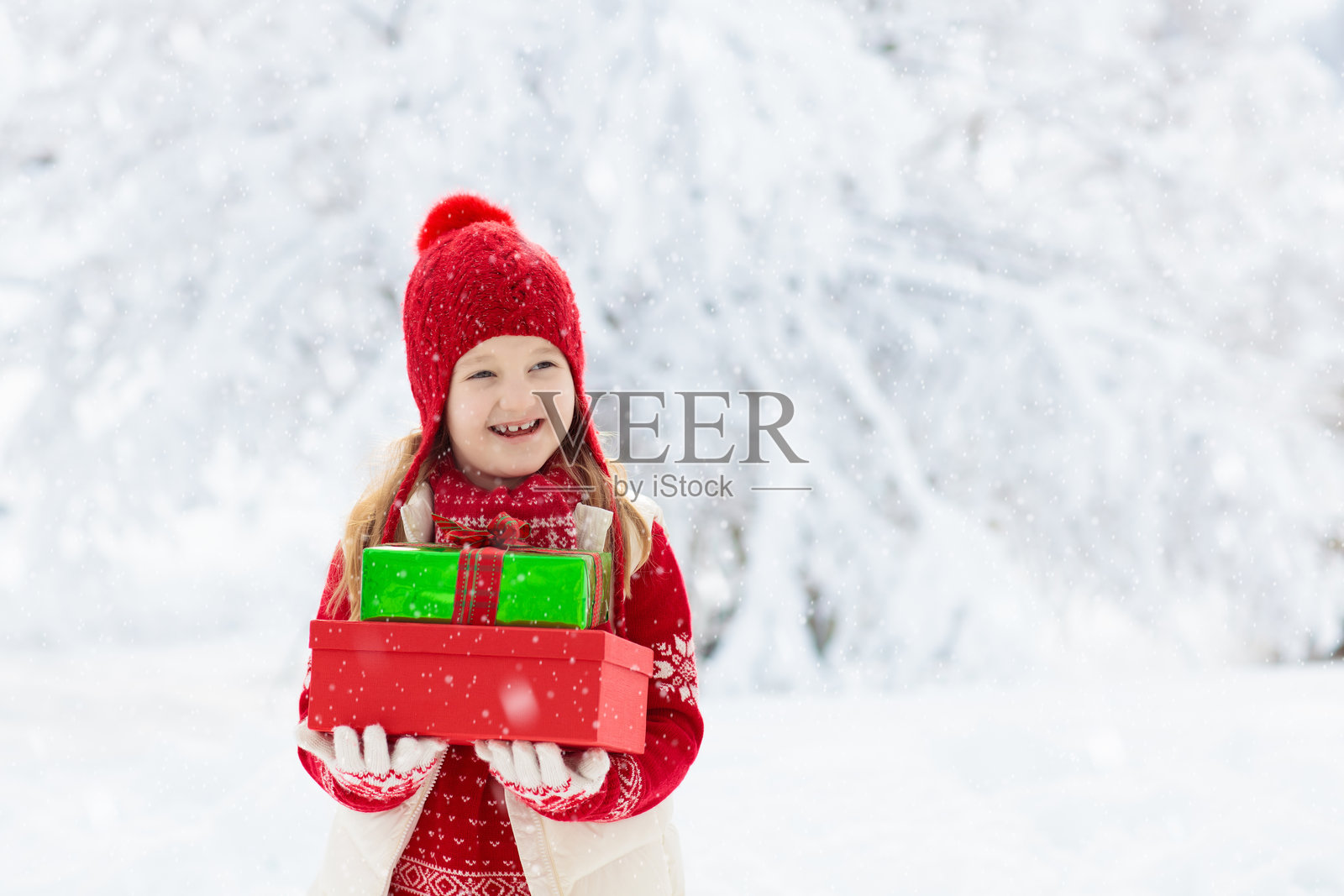 雪中拿着圣诞礼物的孩子。儿童礼物照片摄影图片