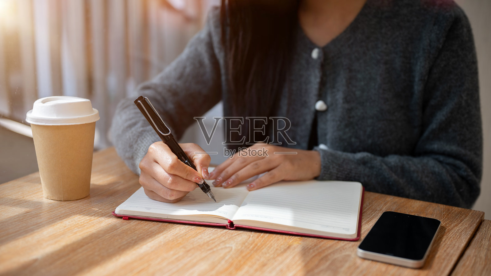 一位女性在咖啡店里坐着,正在书写一本书或日记的裁剪图像。照片摄影图片