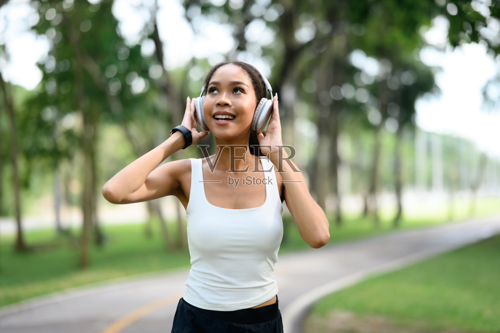 年轻女性穿着运动服,在公园里享受音乐,戴着耳机。照片摄影图片