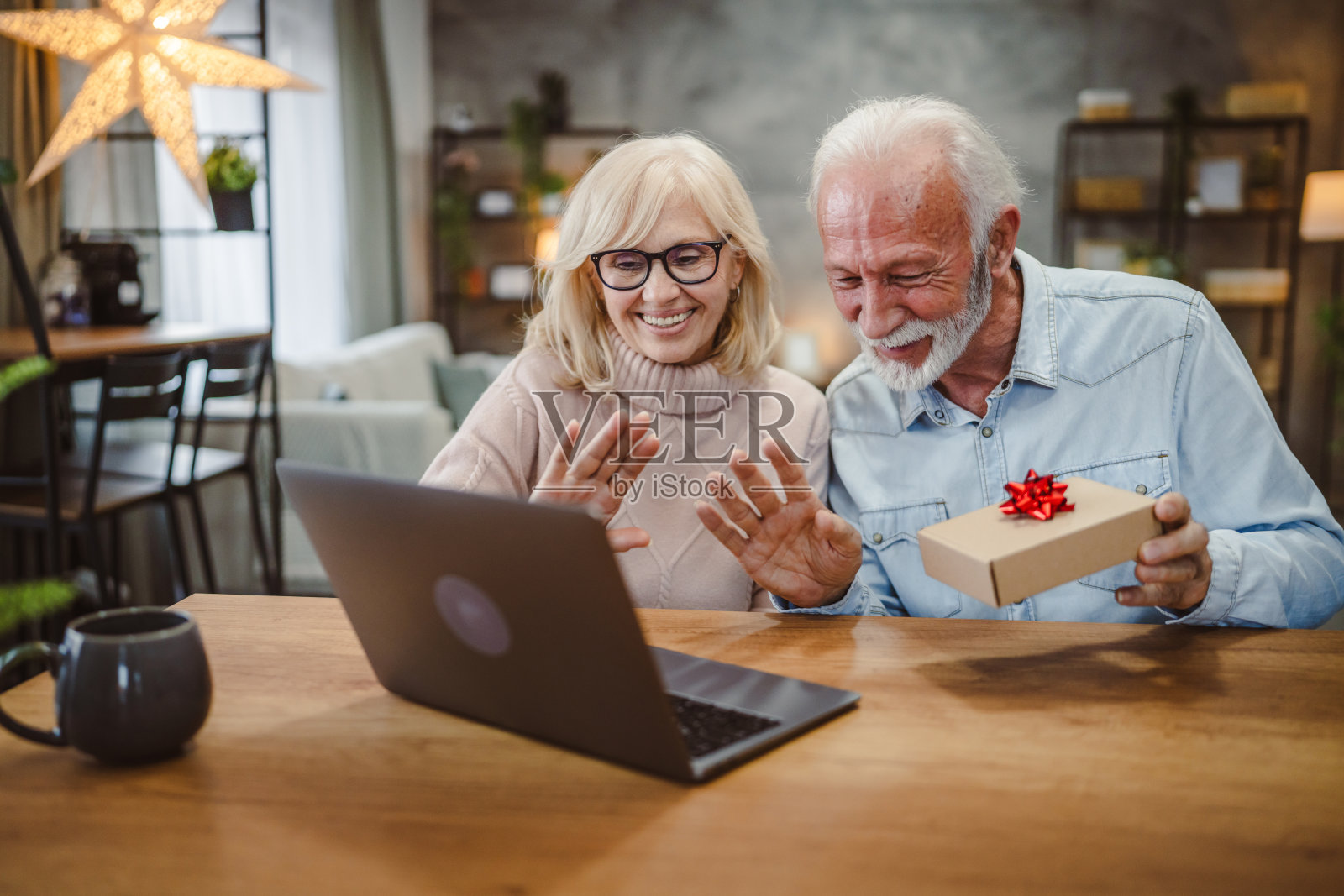 一对兴奋的老年夫妇在笔记本电脑上视频通话时打开礼物照片摄影图片