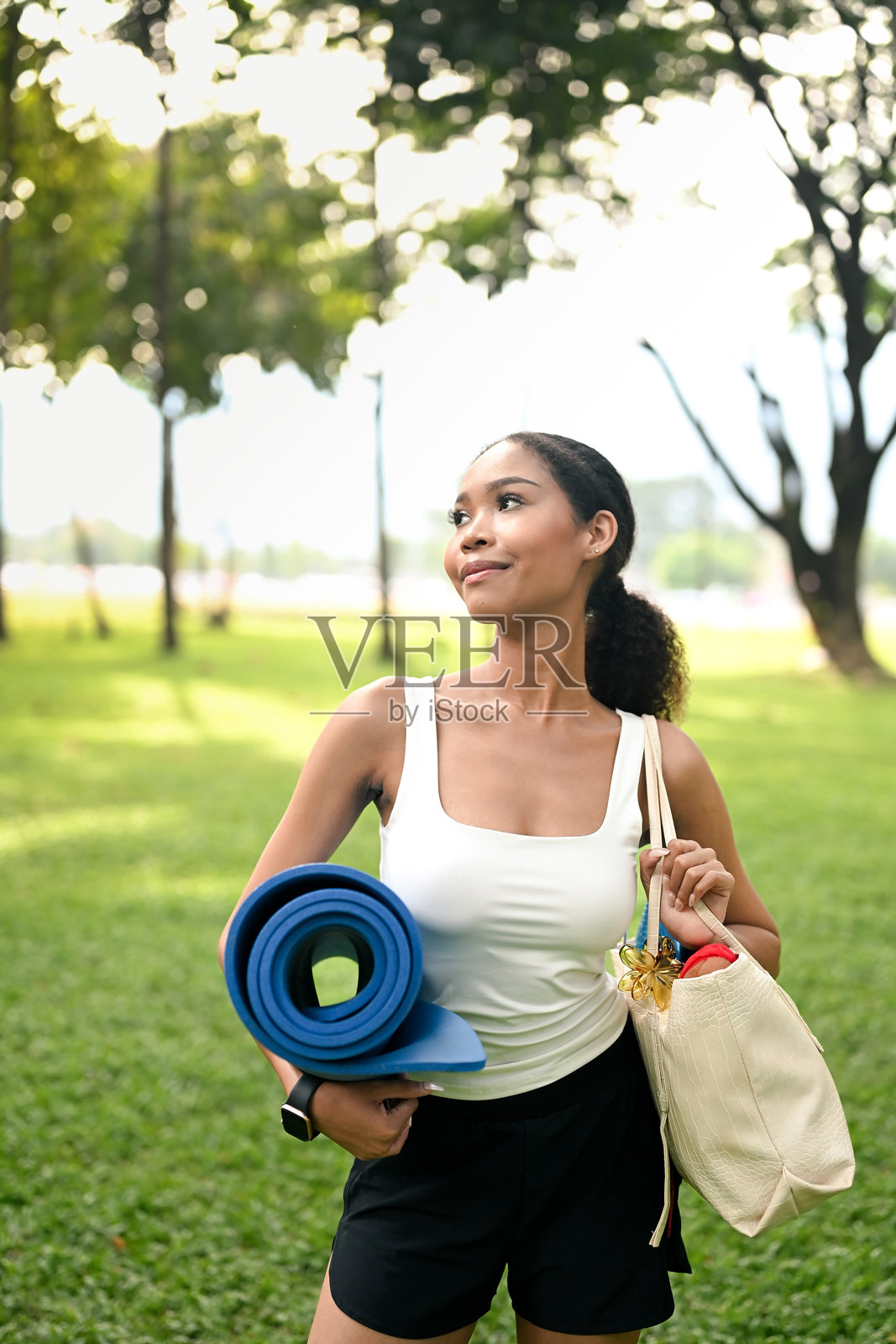 迷人的年轻女性在阳光明媚的公园中手持瑜伽垫照片摄影图片