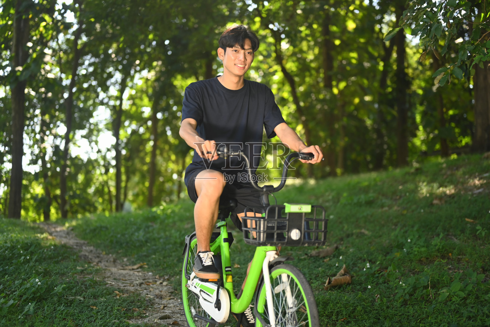 帅气的亚洲男子在阳光明媚的日子里骑自行车穿过宁静的公园。照片摄影图片