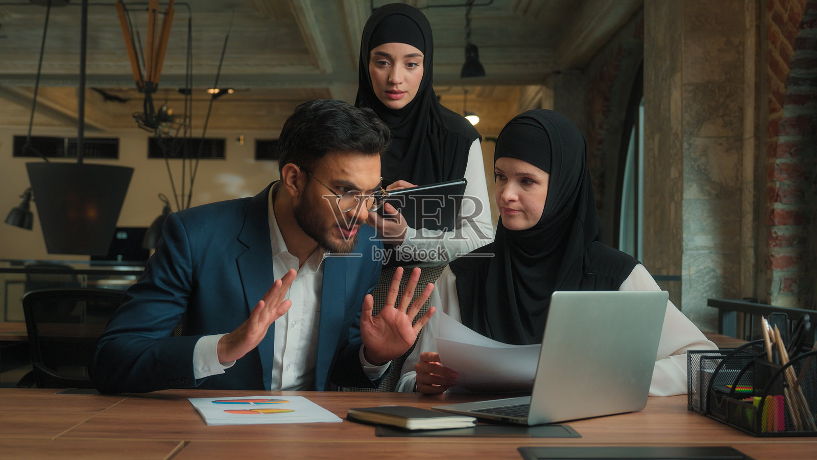 阿拉伯商业团队在办公室工作,穆斯林女性商人和印度男性商人进行视频聊天,在线会议中,领导因销售图表问题而感到愤怒和不满。照片摄影图片