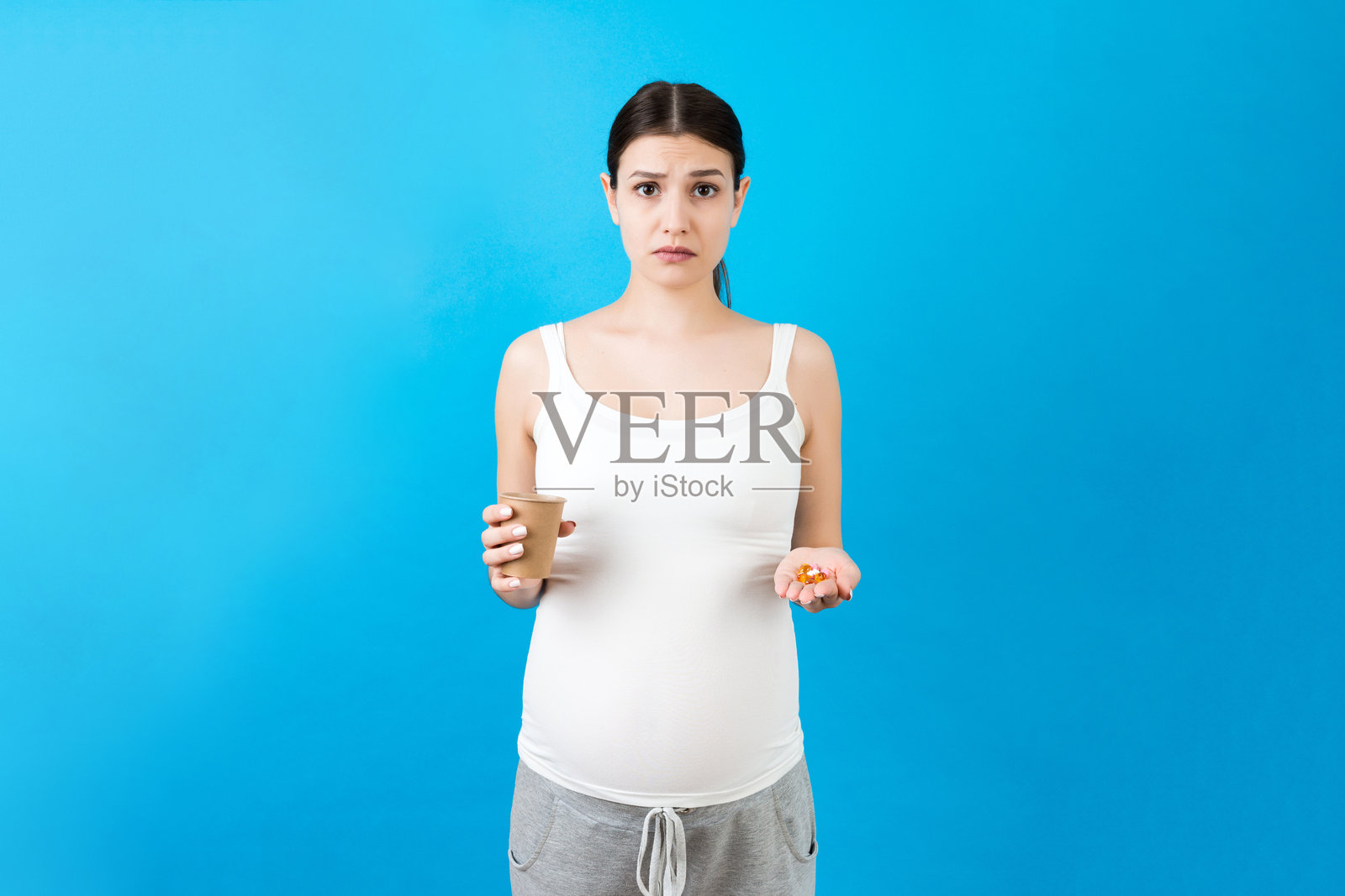 孕妇手中拿着纸杯和一堆药丸,背景色彩丰富,留有空白。医疗保健概念照片摄影图片