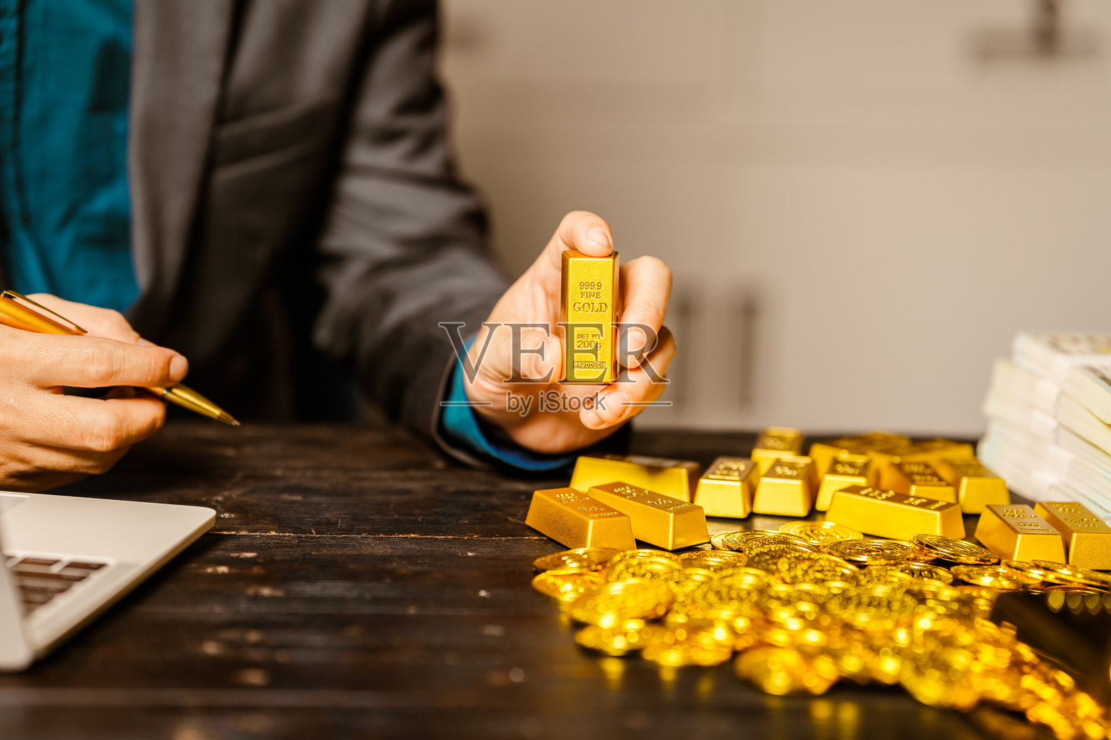 一位商人在夜间办公室的桌子前坐着,使用笔记本电脑分析金条价格、汇率以及黄金交易、采矿和股市的投资计划,面对价格上涨的情况。照片摄影图片