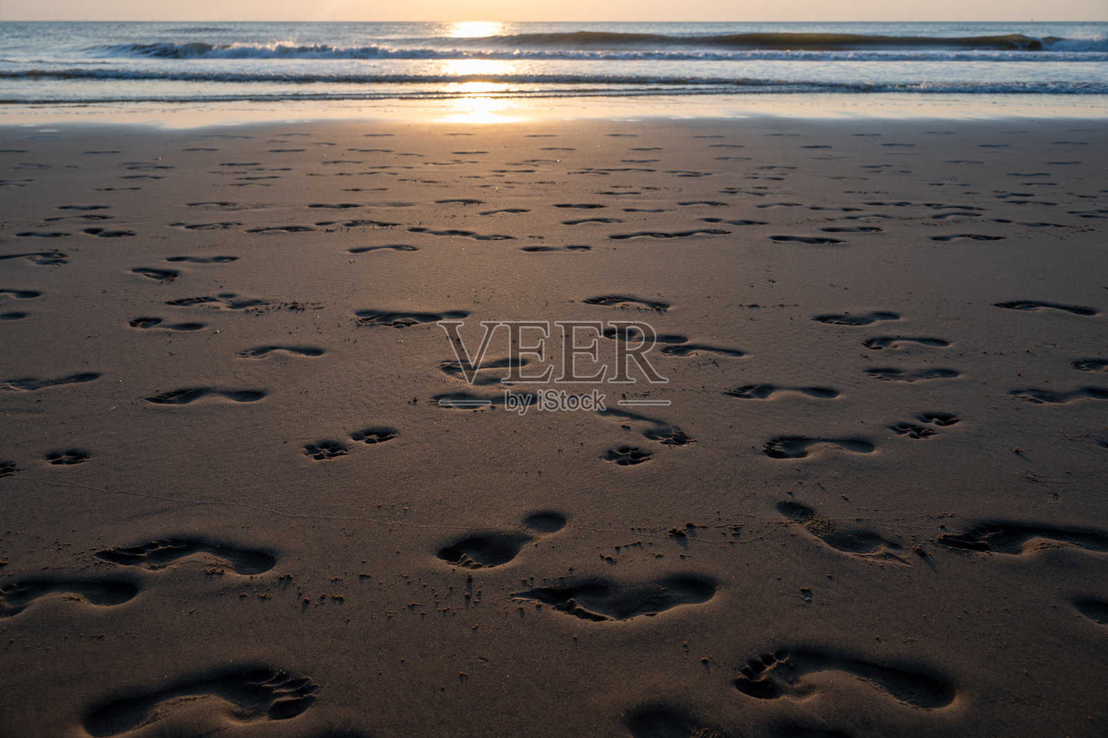 海边沙滩上的脚印,在夕阳的光辉下,海洋与阳光交相辉映照片摄影图片