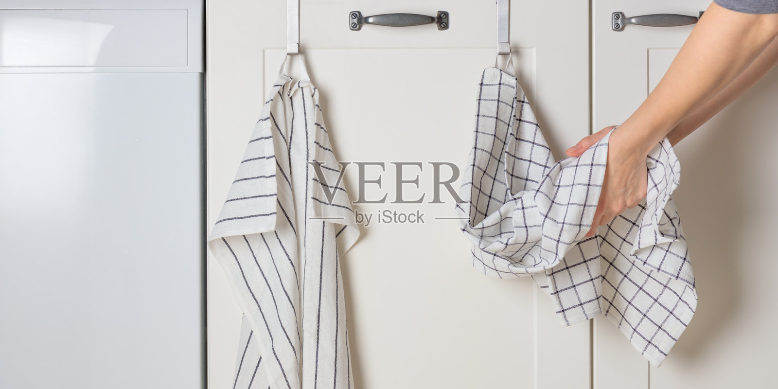 一位年轻女性正在厨房用挂在橱柜门上的棉毛巾擦干双手。照片摄影图片