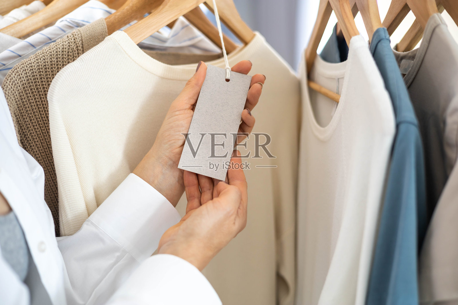 女性手握着一张空白白色标签,背景是中性色调的针织衣物。照片摄影图片
