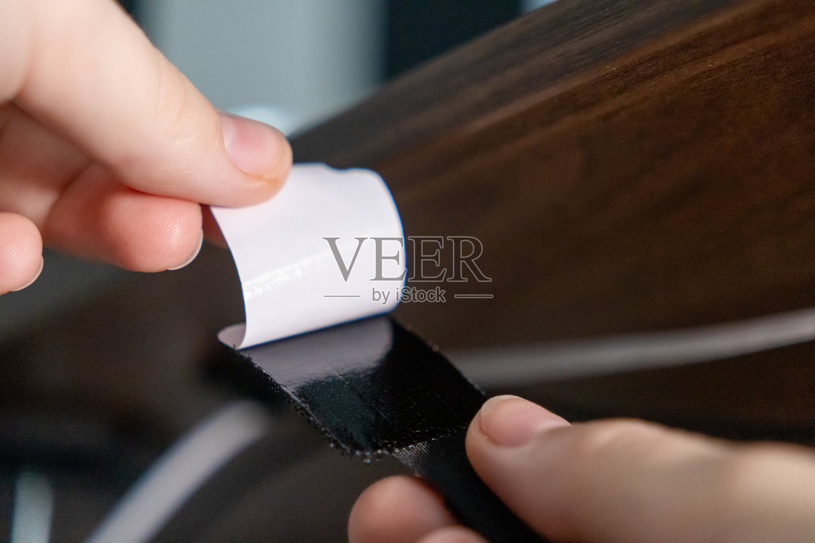 手动撕下魔术贴带的粘性背面,将其固定在木桌下以整理电缆。照片摄影图片