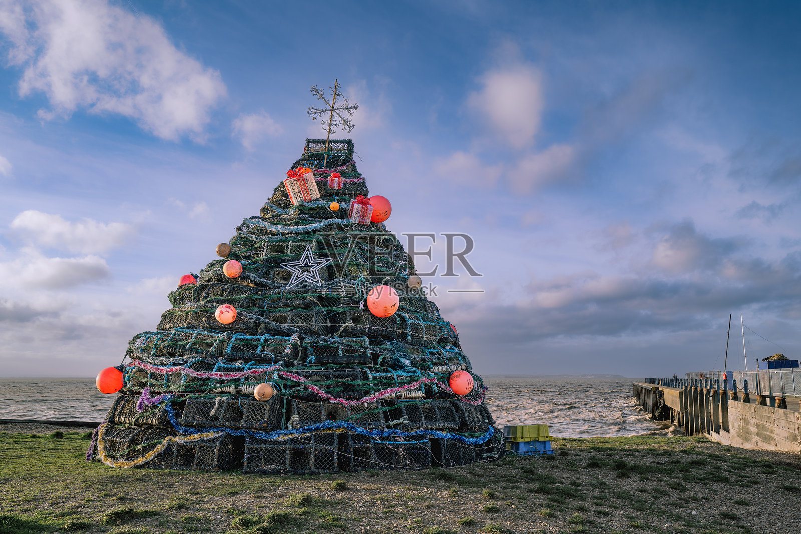 在英国肯特郡惠茨特布尔港口附近的海滩上,用渔网筐、龙虾篮和浮标制作的圣诞树。照片摄影图片
