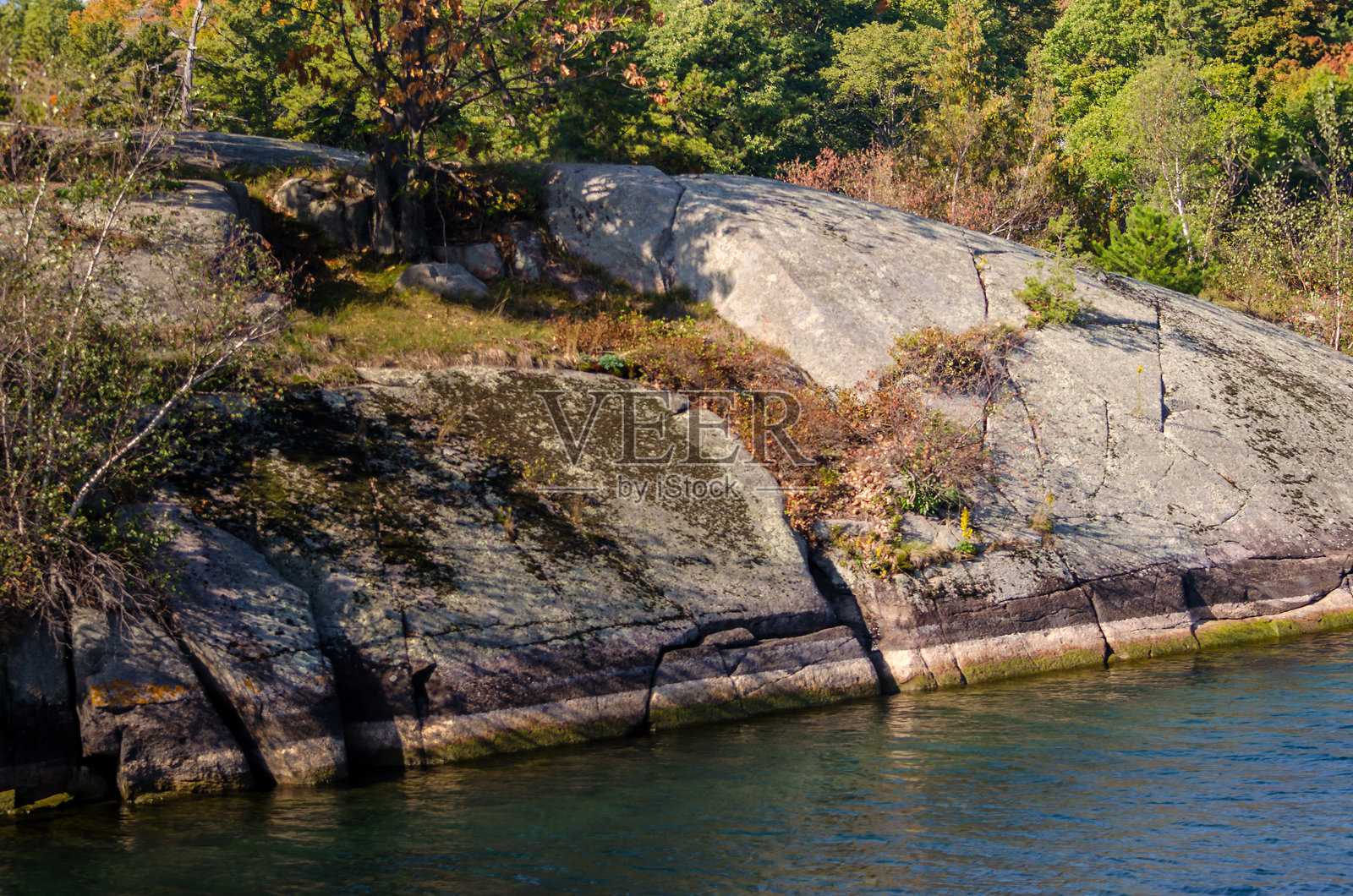 岛屿的岩石海岸向水边倾斜。照片摄影图片