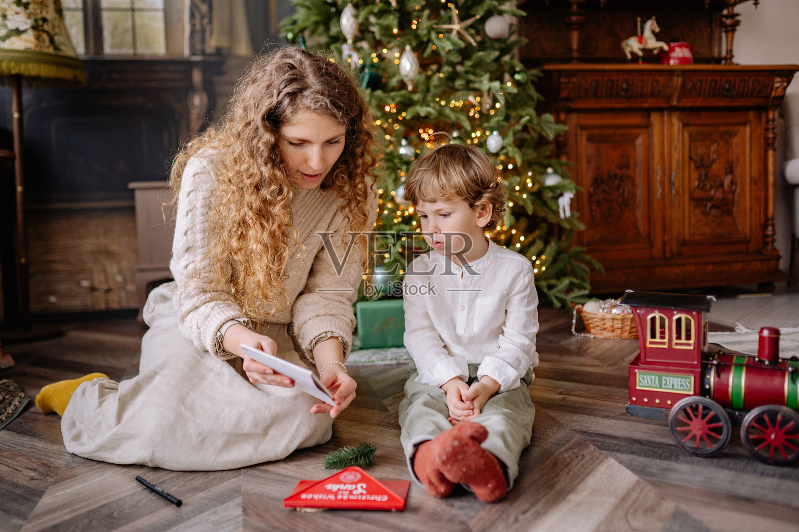 圣诞庆祝活动,捕捉到一位母亲在装饰树旁帮助她的儿子进行节日项目,周围环绕着节日装饰。照片摄影图片