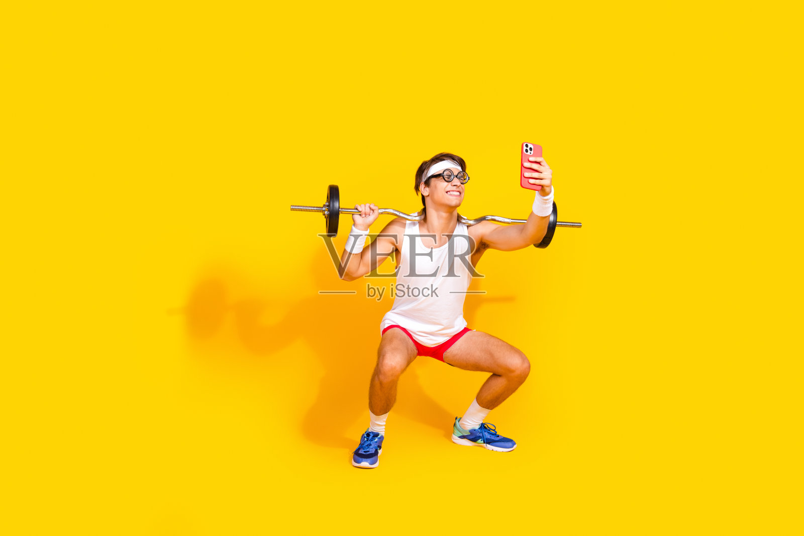 穿着运动服的快乐年轻人在黄色背景下举着杠铃自拍锻炼。照片摄影图片