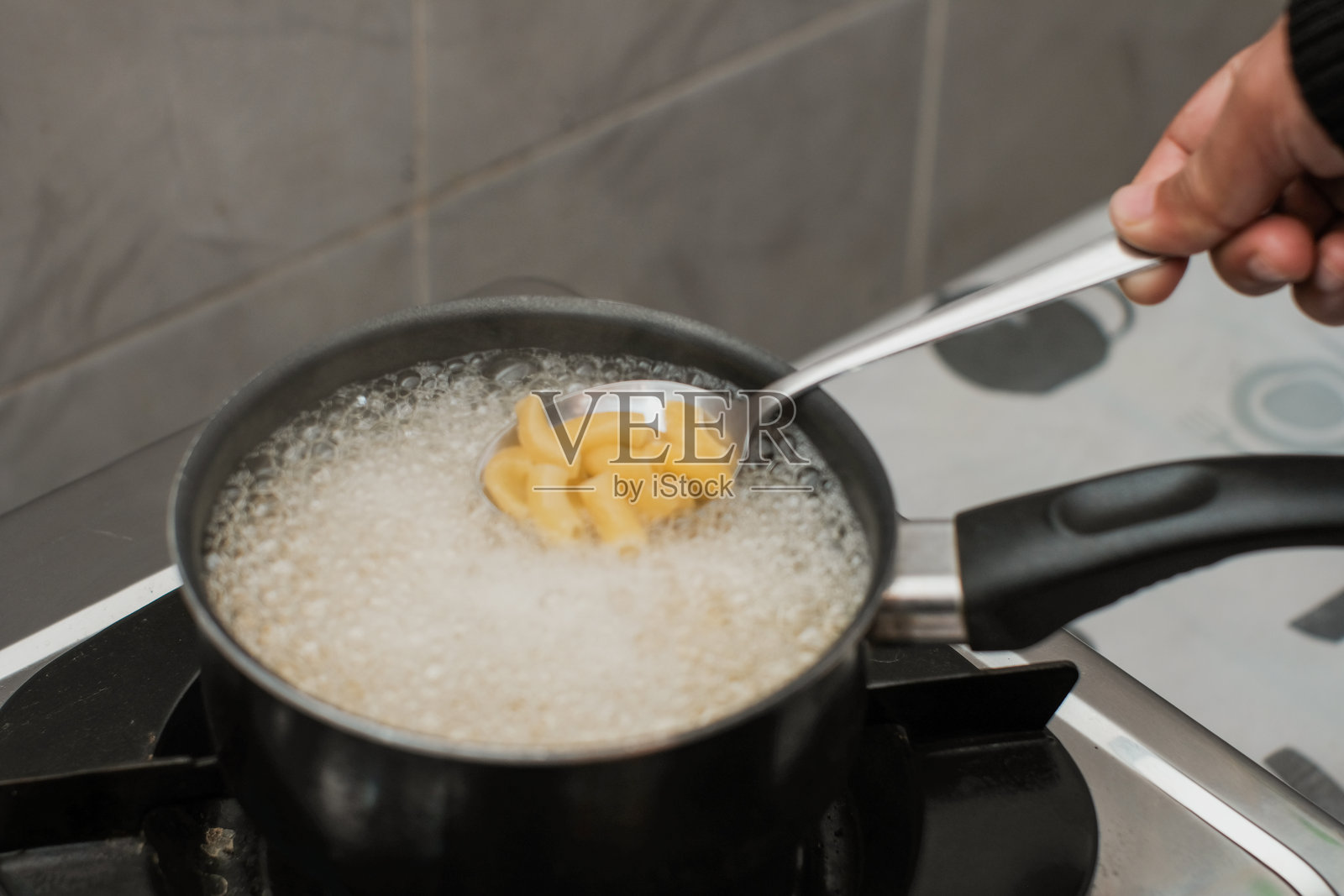 一位女性在锅中用沸水煮意大利通心粉或笔管面。照片摄影图片