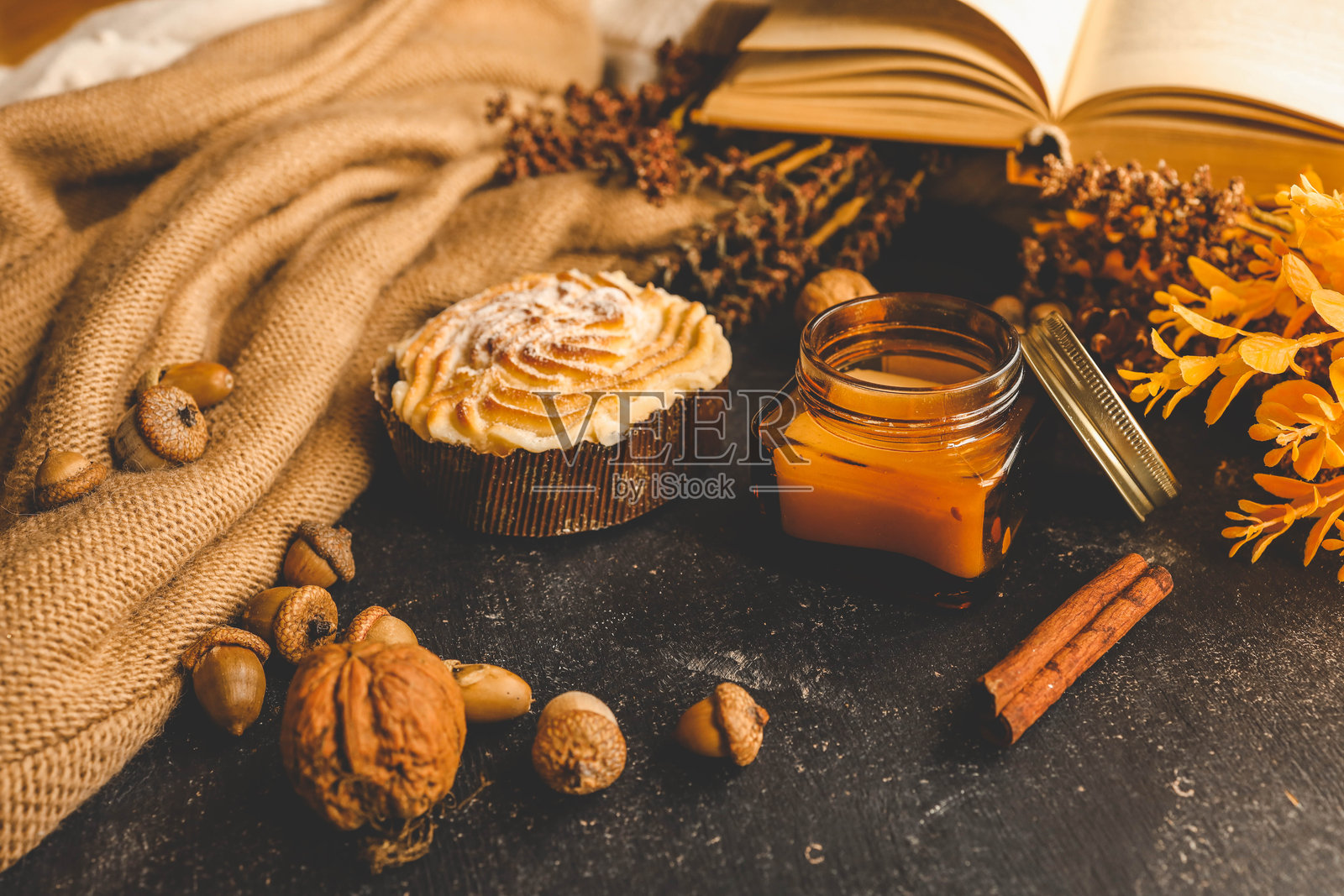 秋季组合:杯子蛋糕、瓶装蜡烛、橡果和胡桃,背景是温暖的针织面料和干燥植物。照片摄影图片
