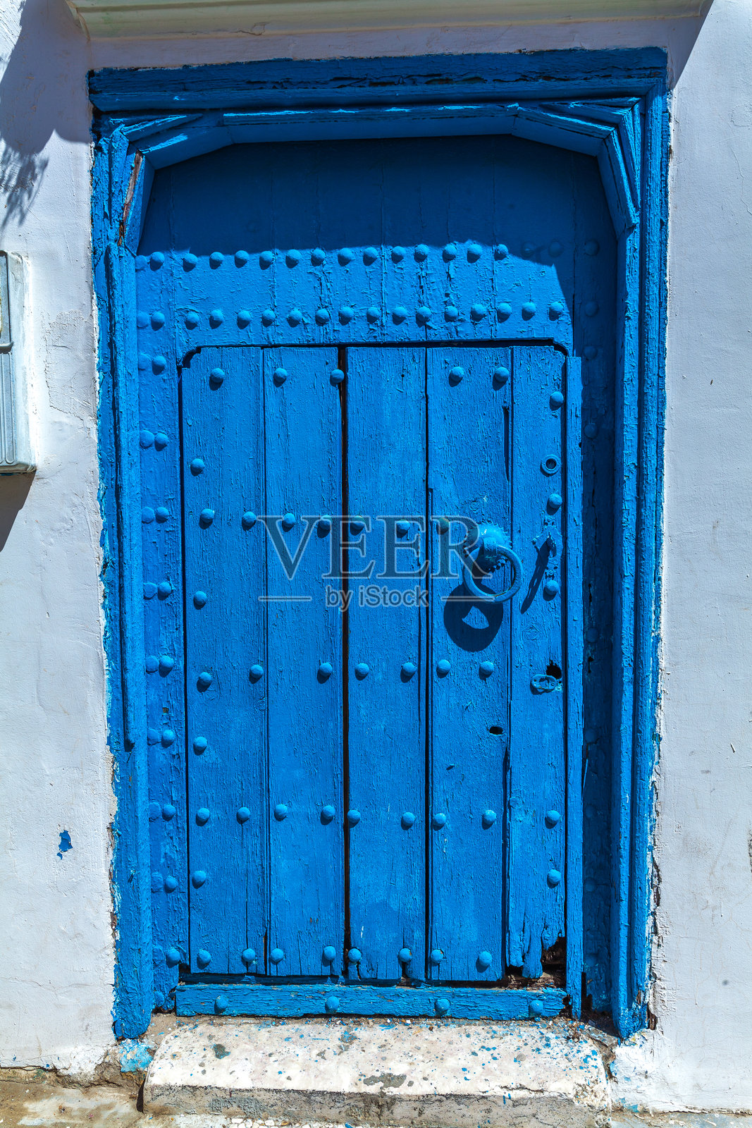 风化的木门涂成鲜艳的蓝色,装饰着金属铆钉和环形拉手,形成一个视觉丰富且质感独特的历史建筑入口。照片摄影图片