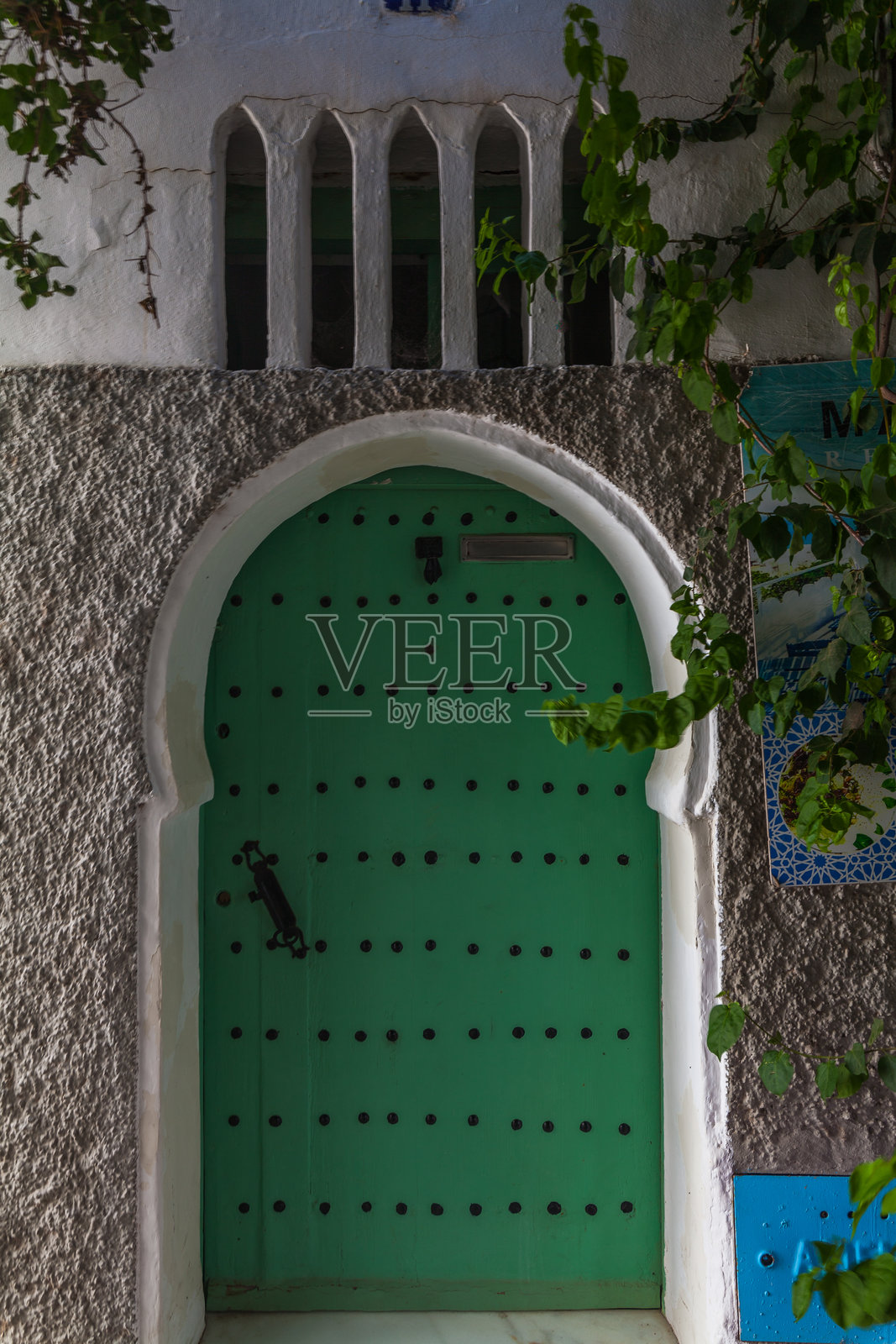 生动的绿色木门被白色粉刷的墙壁框住,墙上有一系列拱形壁龛,形成一个风景如画的入口,融合了建筑细节和自然元素。照片摄影图片