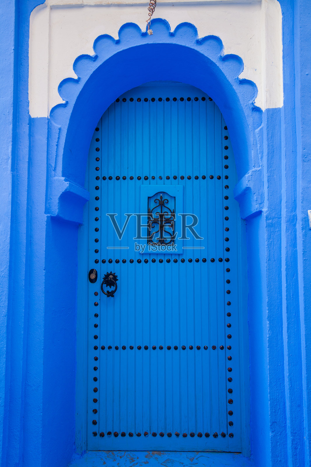 蓝色拱形木门,装饰性铆钉和一个小巧精致的窗户,背景是蓝白相间的墙壁照片摄影图片