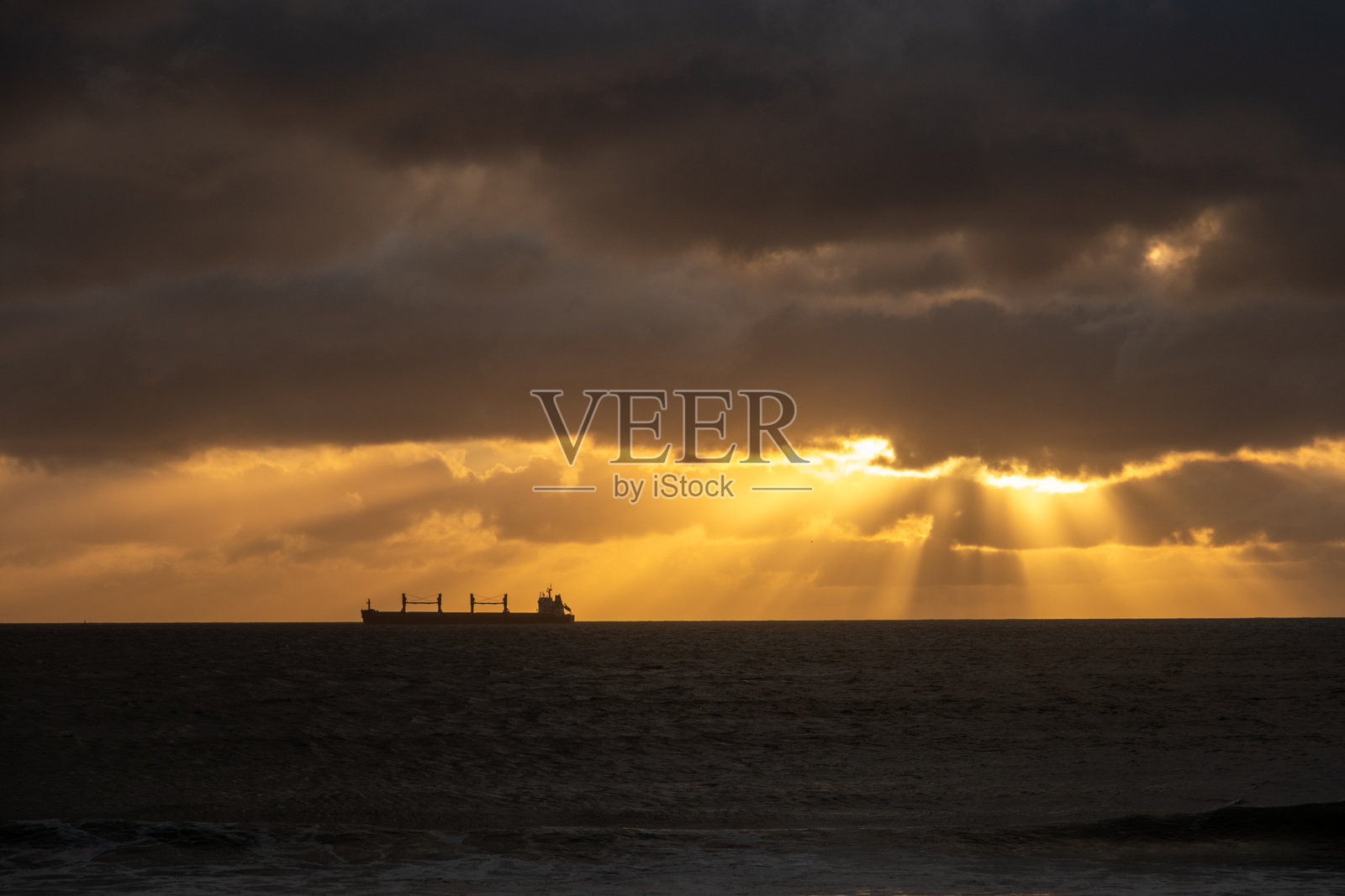 日落时分,水面上的货船与光线射线照片摄影图片